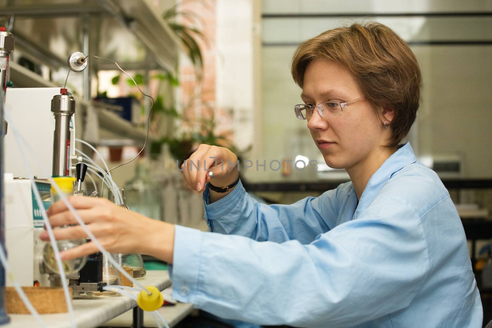 The young nice woman-scientist work with syringe on a background scientific instruments