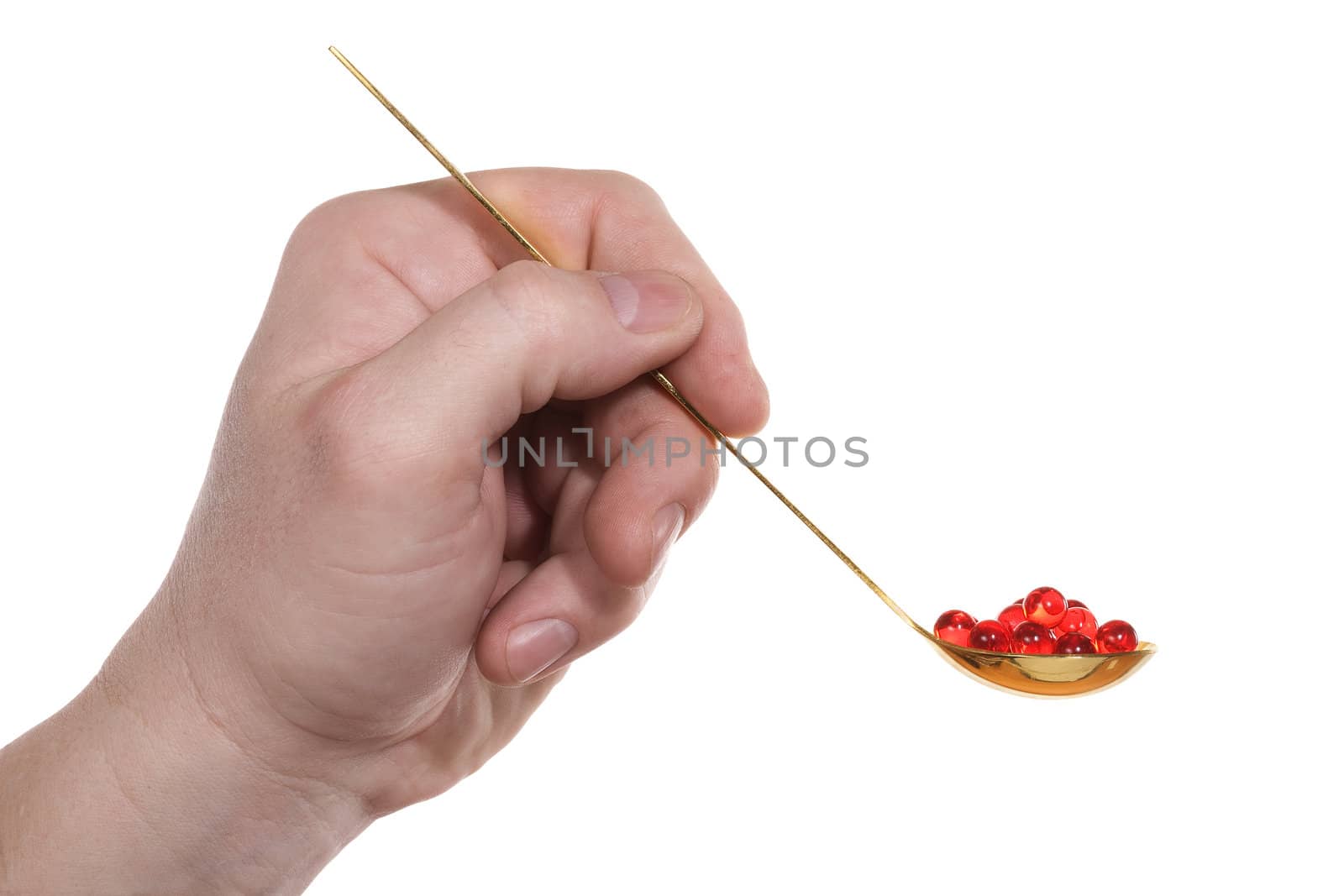 The hand holds a teaspoon with red pills. Isolated on white [with clipping path].