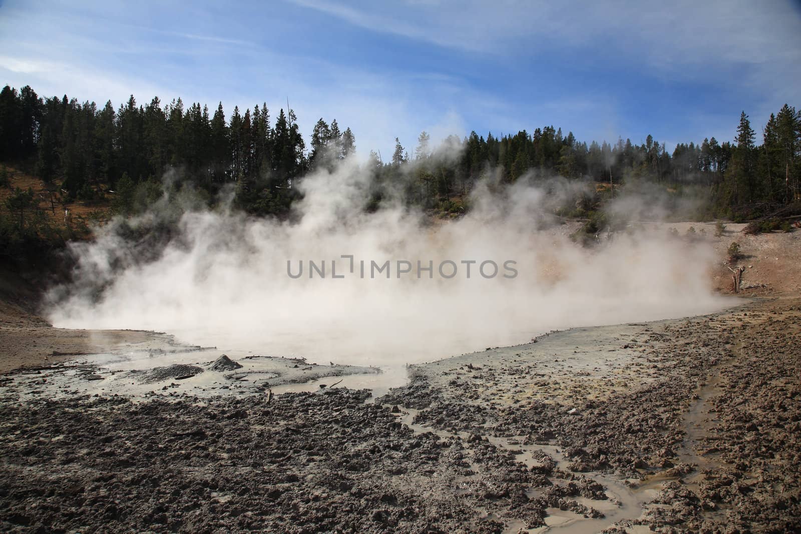 Steaming pools of muddy water in front of a mountain landscape.