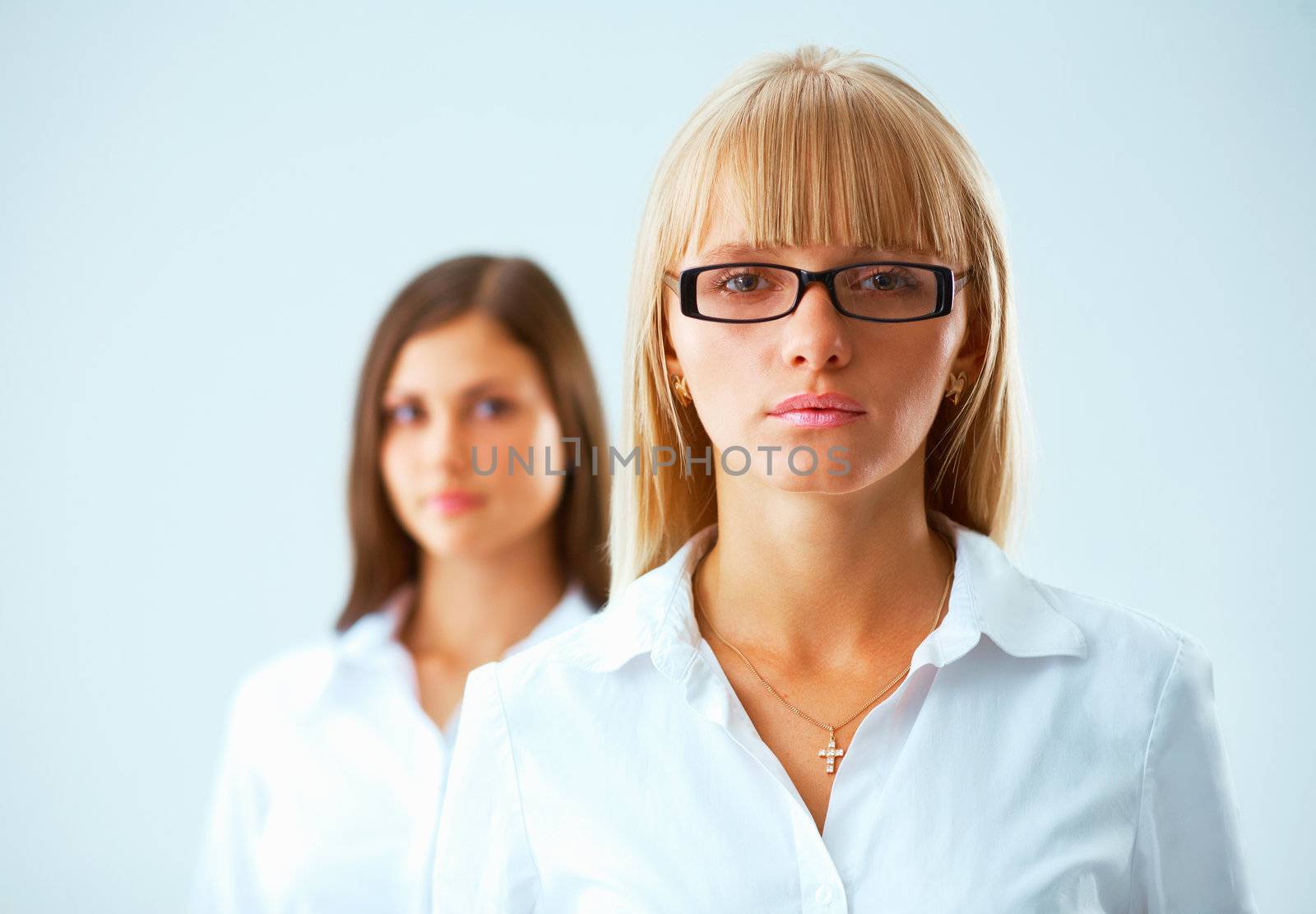 Two young  serious business women on light blue background whith a fair hair woman in focus