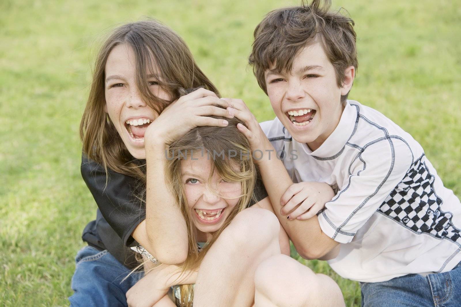 Three young siblings wrestling outdoors on the grass