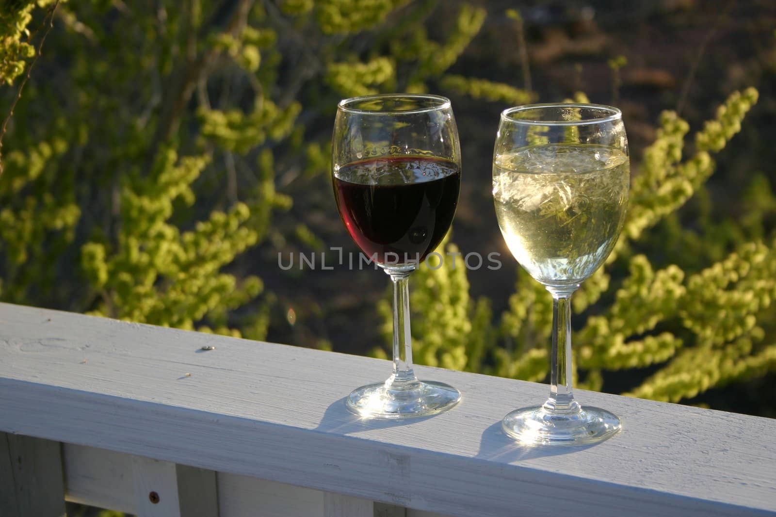 A glass of red wine and a glass of white wine sit on a porch railing ready to provide refreshment and relaxation after a stressful day.