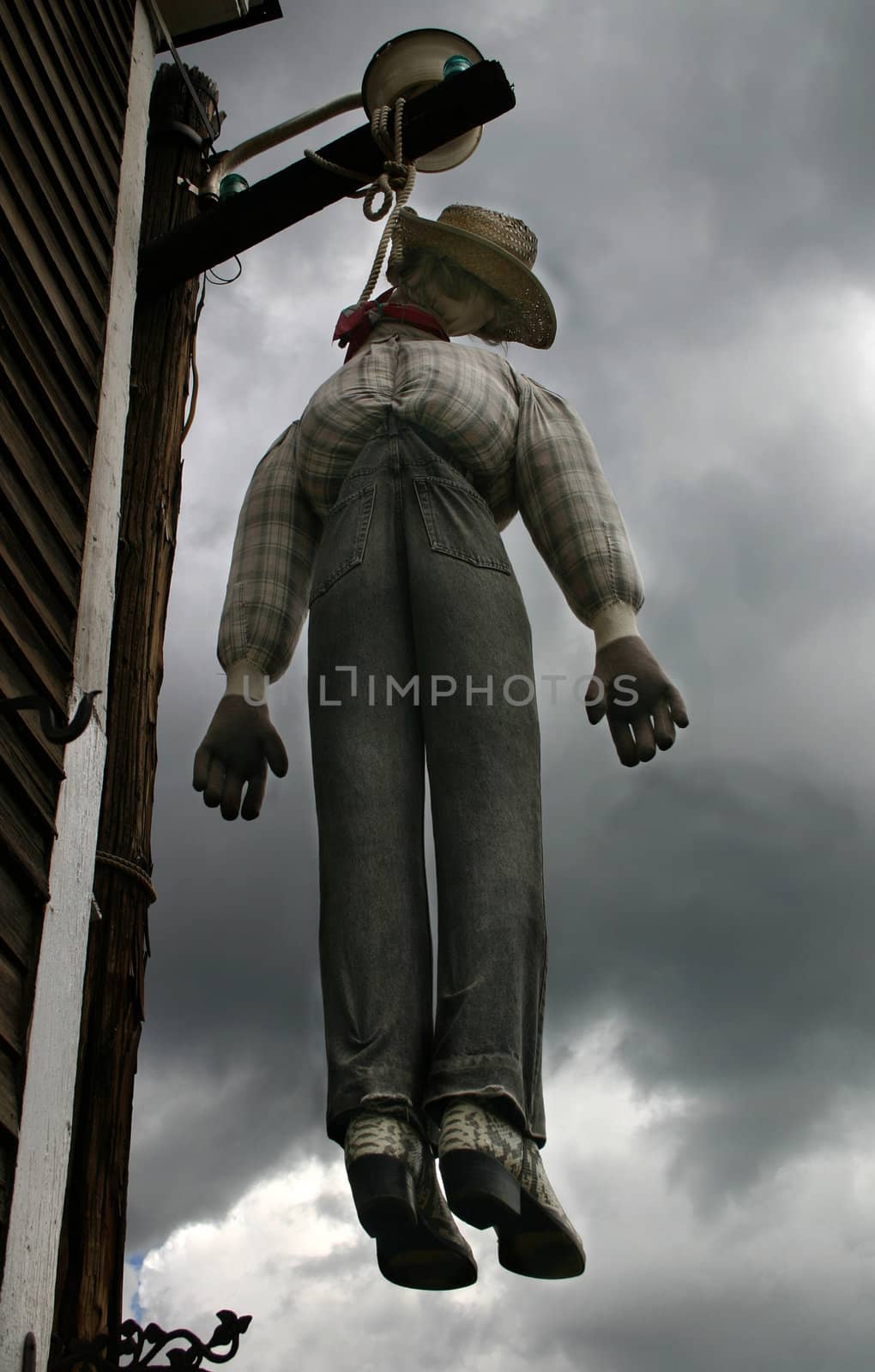 Spooky figure hanging from beam against an ominous, dark, cloudy stormy sky.