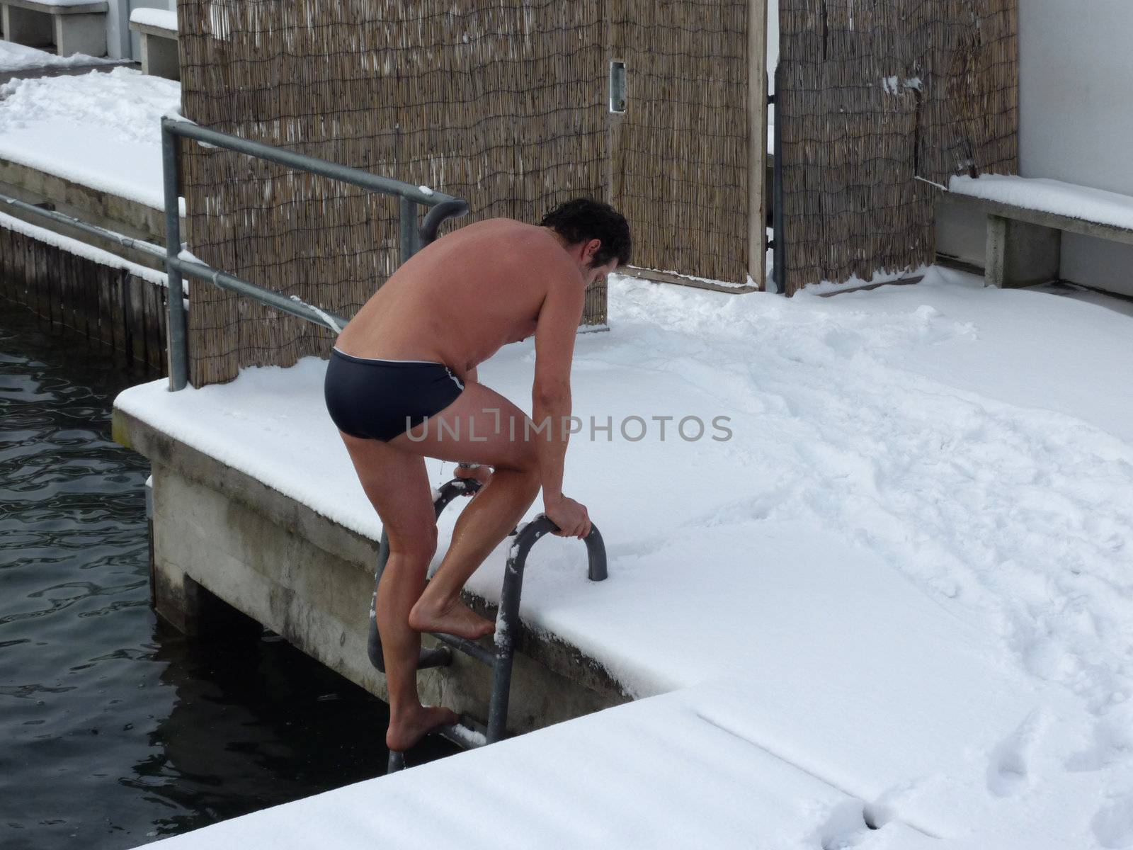 Swimmer getting out of the lake water by a ladder during winter time