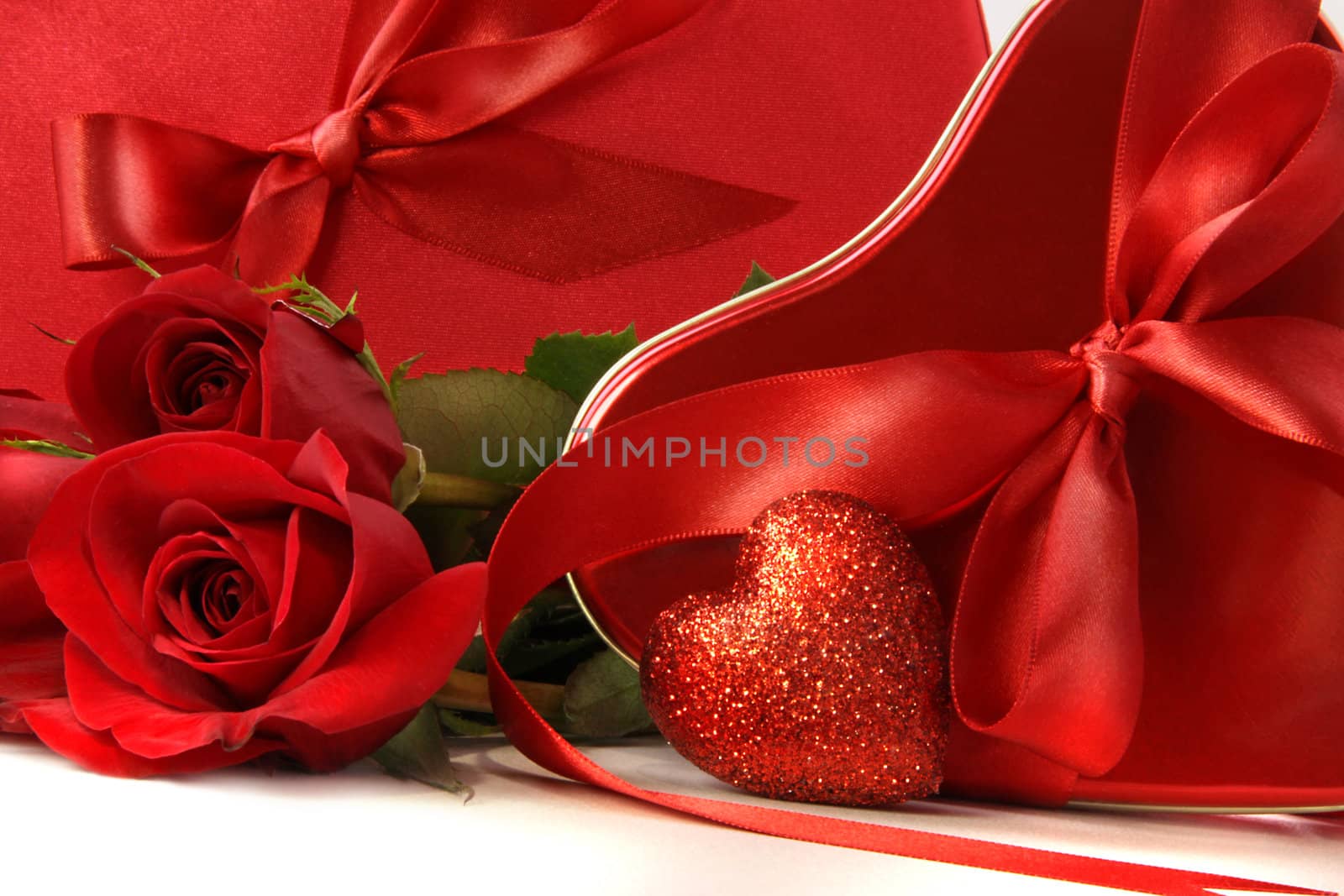 Chocolate boxes with red satin ribbons and roses on white background