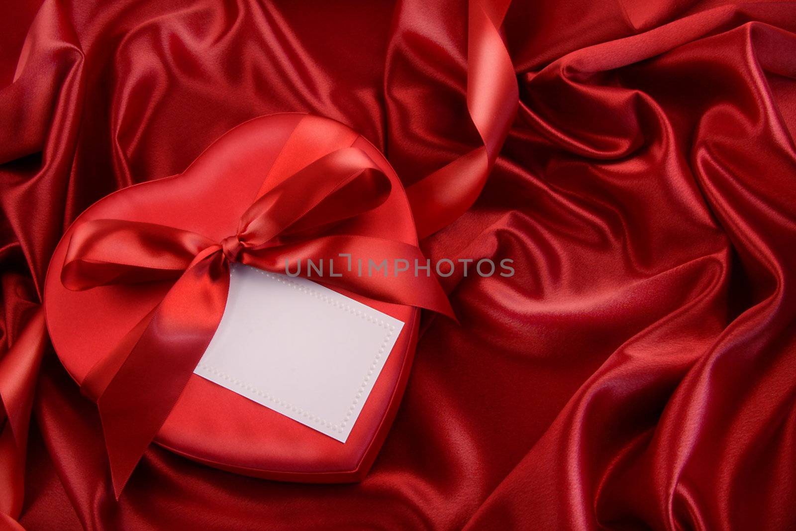 Box of chocolate with red ribbon on satin