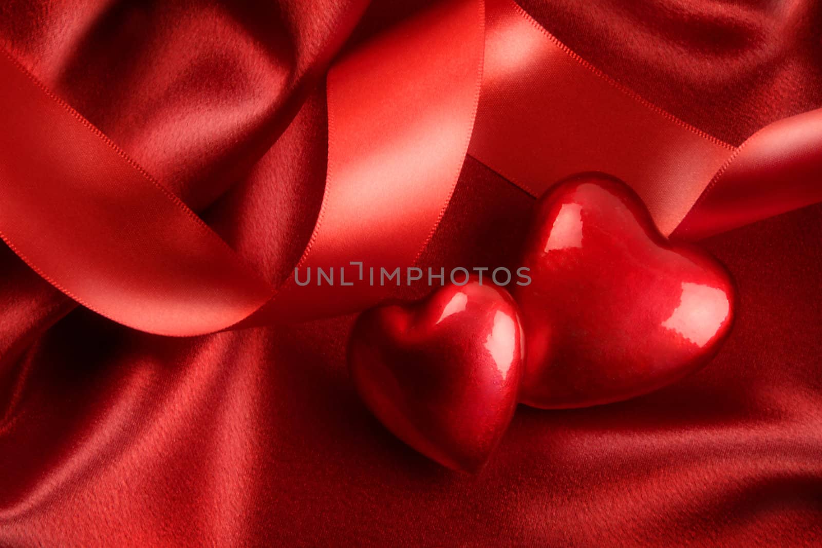 Two red hearts with ribbon on satin background
