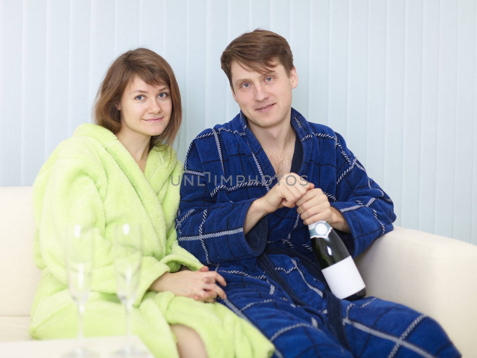 Young happy couple in dressing gowns drinks sparkling wine