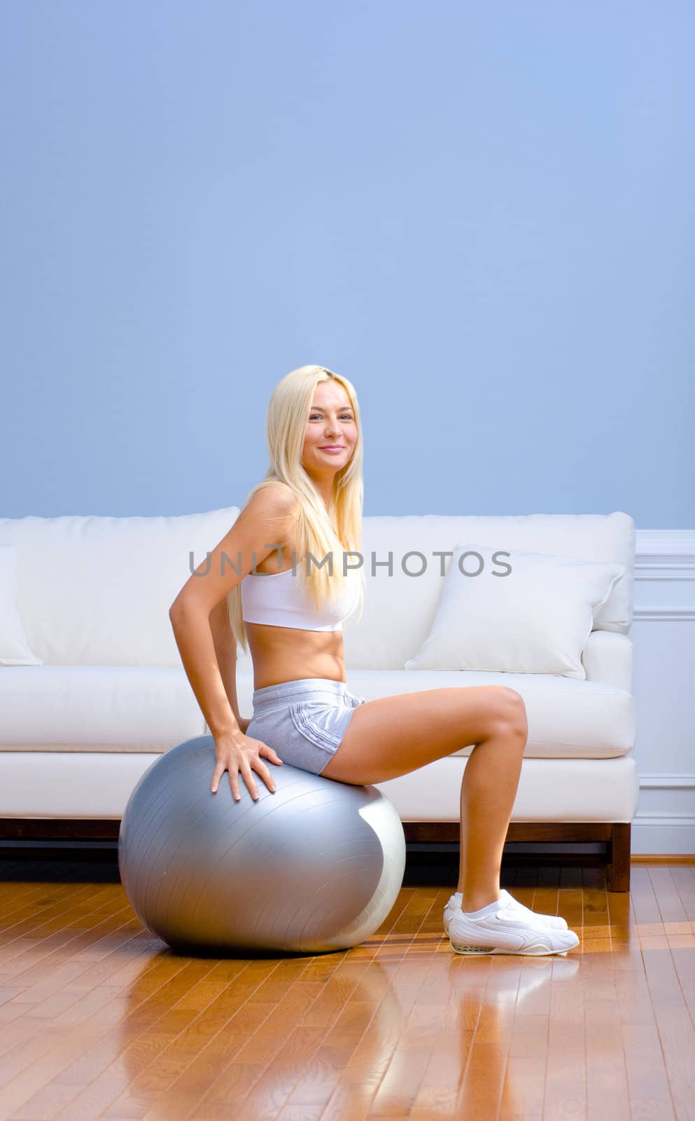 Young woman sits on an exercise ball in the living room. She is dressed in sportswear. Vertical shot.