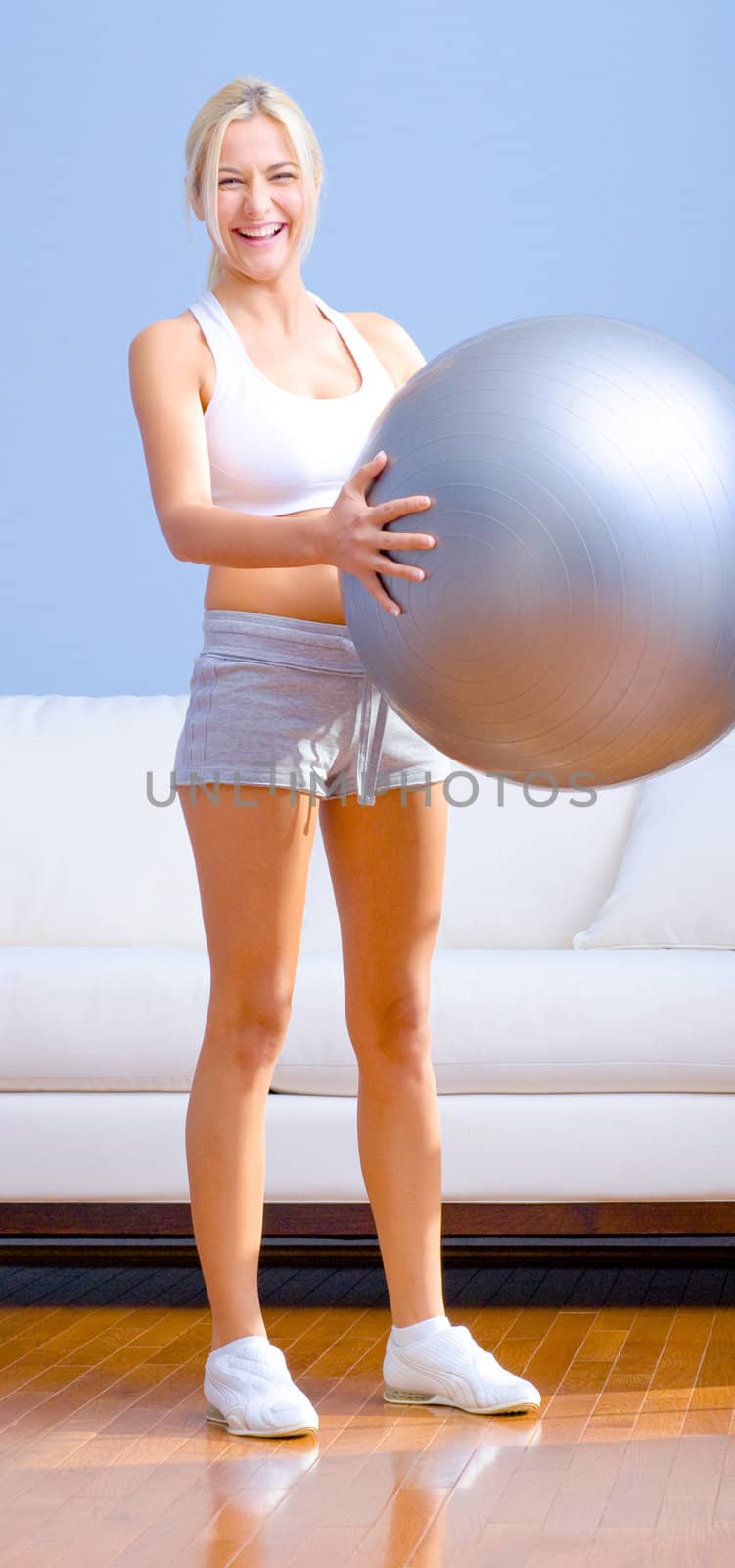 Young woman wearing sportswear holds a balance ball in a living room.  Vertical shot.