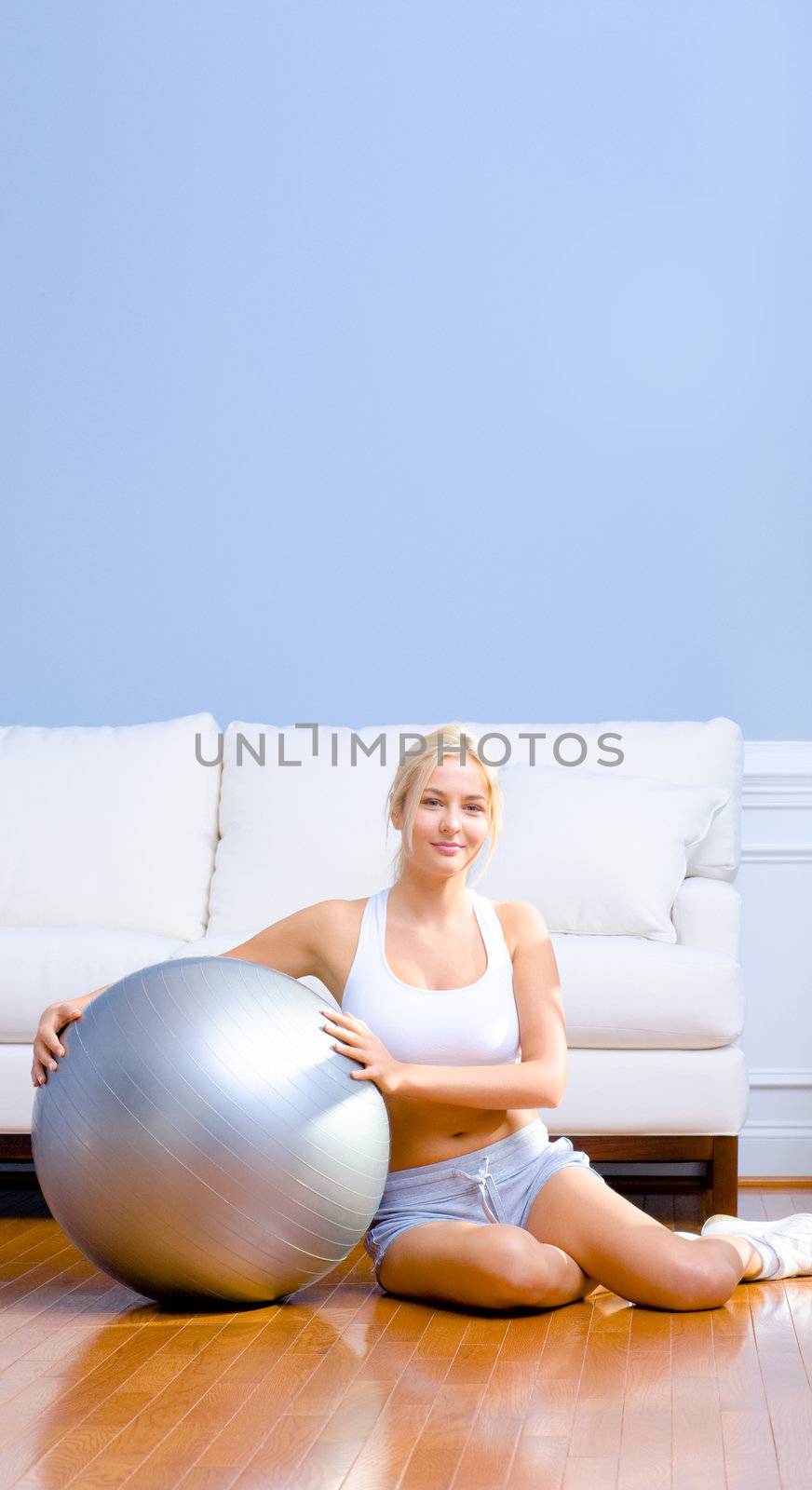 Young woman in sportswear sits next to an exercise ball in her living room.  Vertical shot.