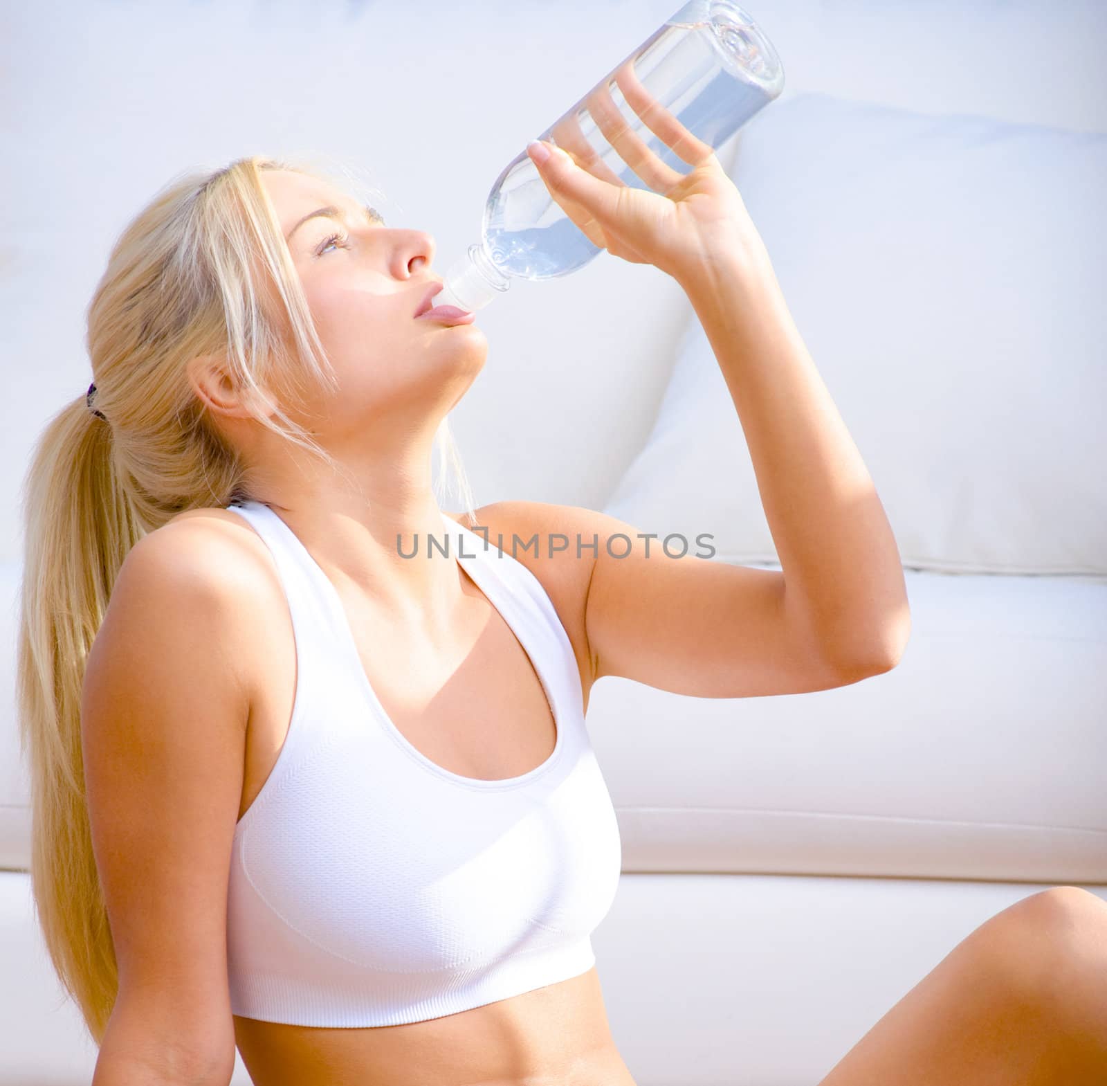 Side view of a young woman in sportswear drinking bottled water.  Square shot.