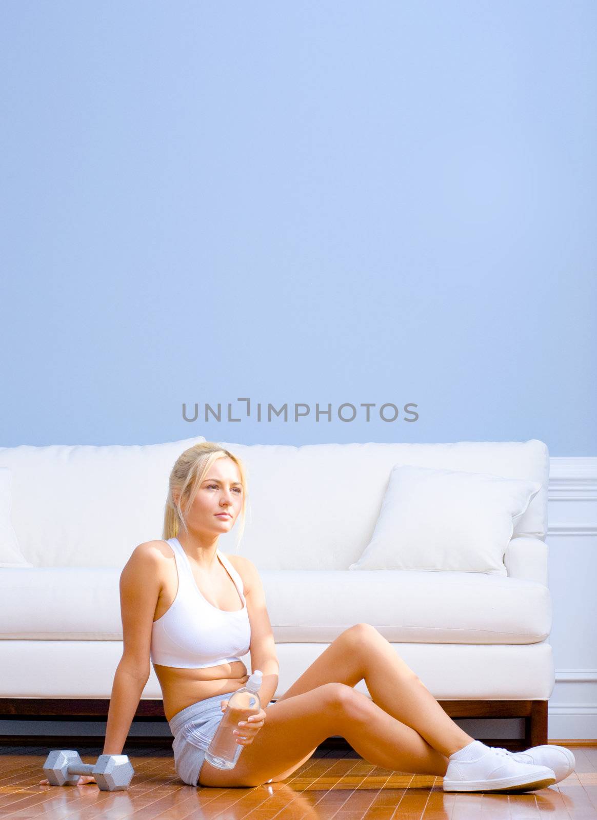 Young woman sitting in a living room after exercising with a hand weight and bottled water. Vertical shot.