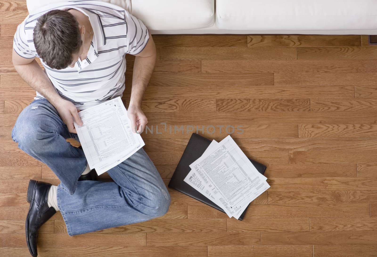 Young man sits on the floor as he looks through paperwork. Horizontal shot.