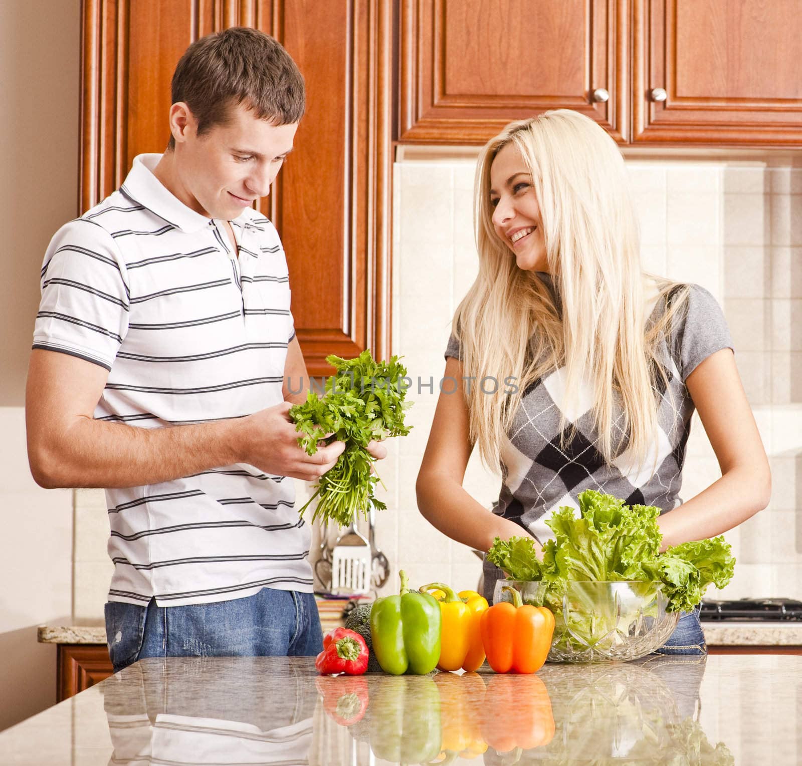 Young couple in the kitchen enjoy making a salad with fresh vegetables. Square shot.