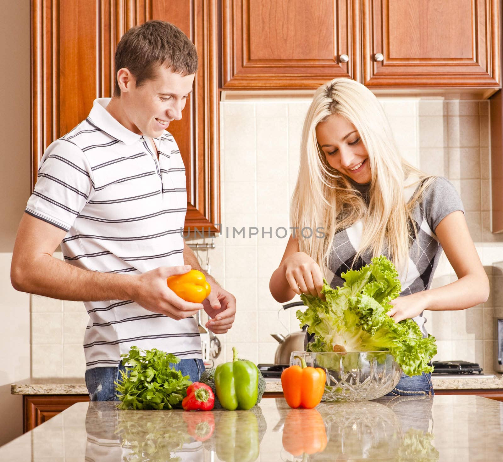 Young couple in the kitchen enjoy preparing salad with fresh vegetables. Square shot.