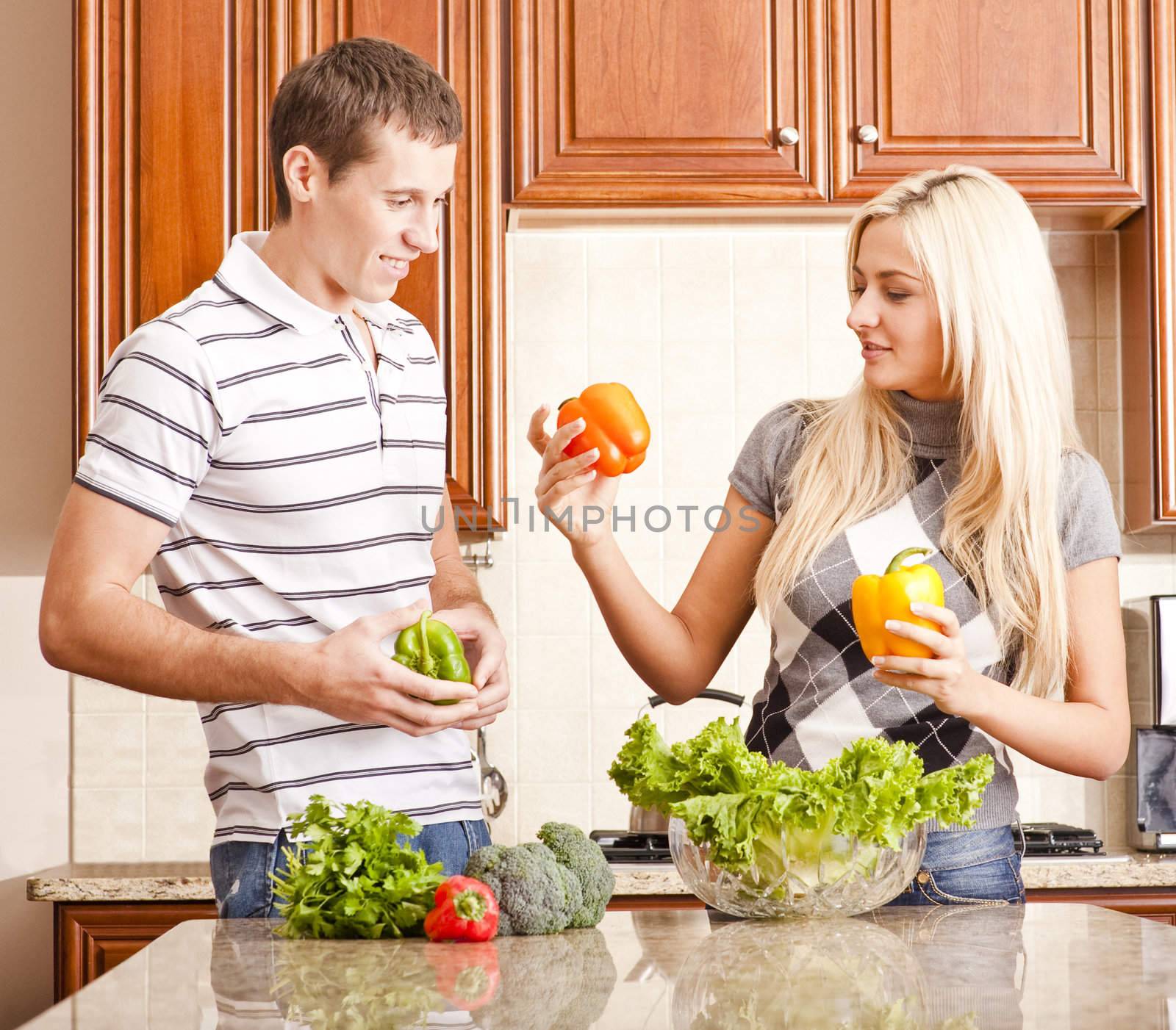 Young couple in the kitchen inspect peppers for their salad. Square shot.