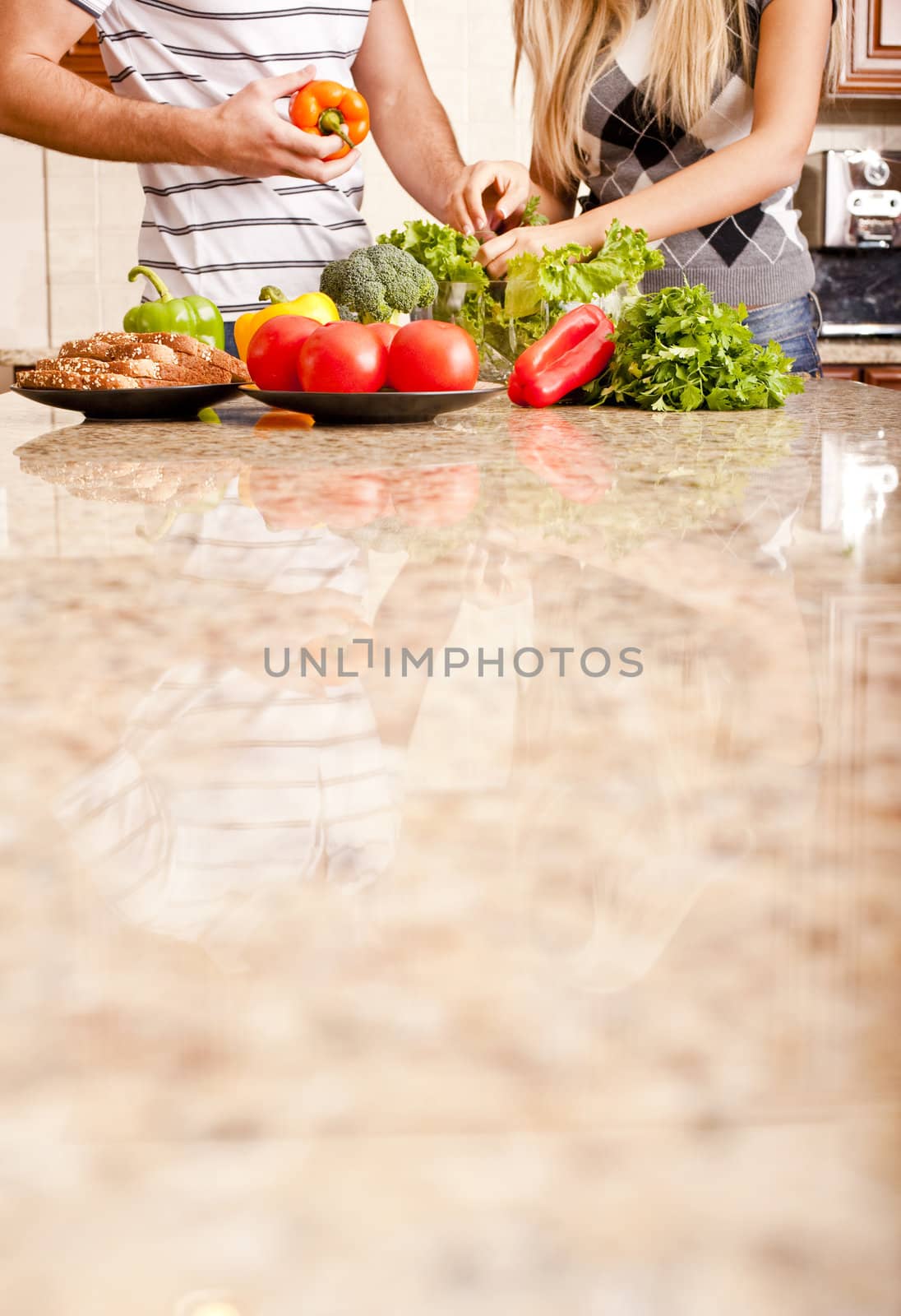 Young couple picks through fresh vegetables at the far end of a kitchen counter. Vertical shot.