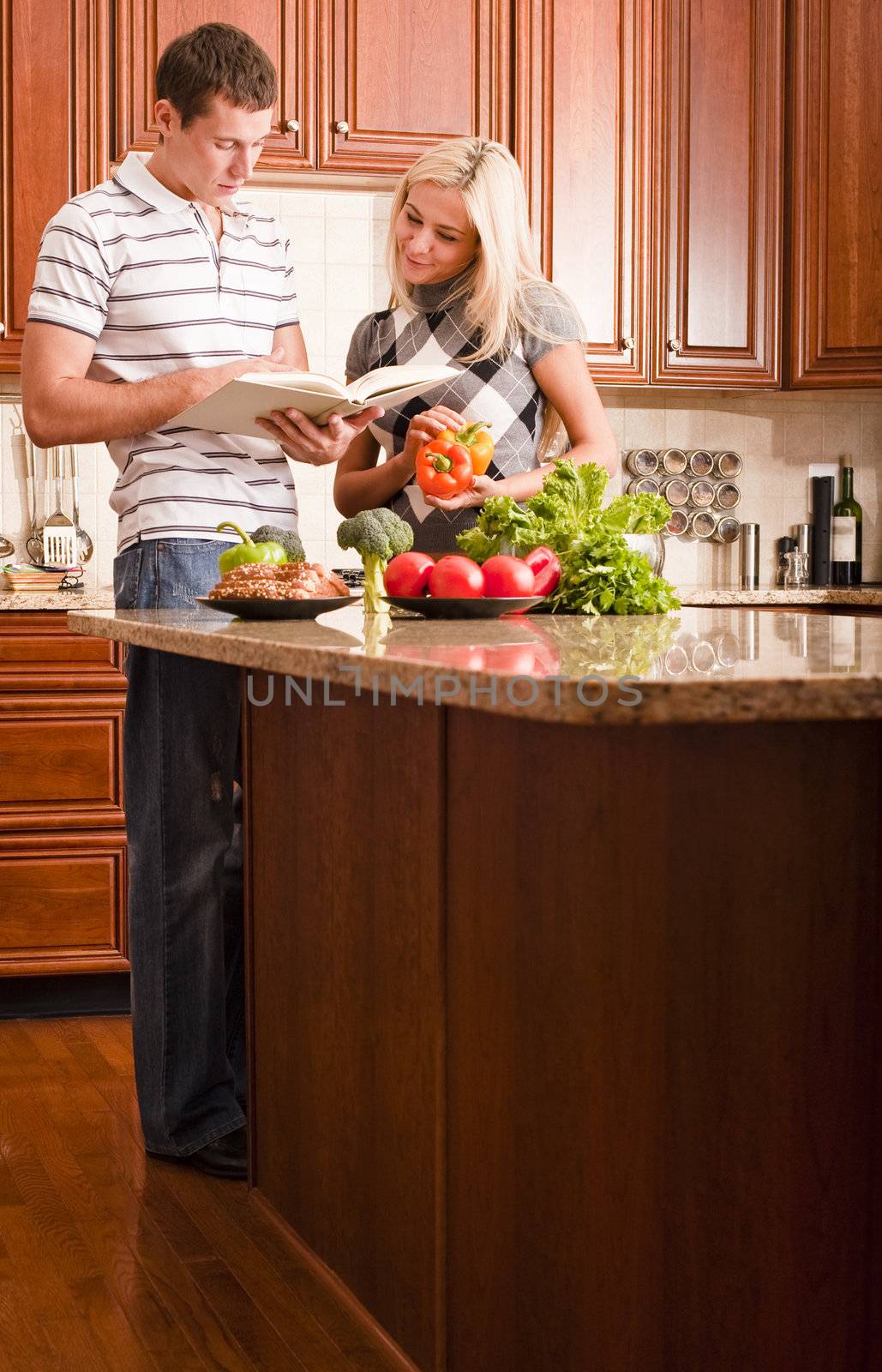 Young couple read through a recipe book in the kitchen with a counter full of fresh vegetables. Vertical shot.