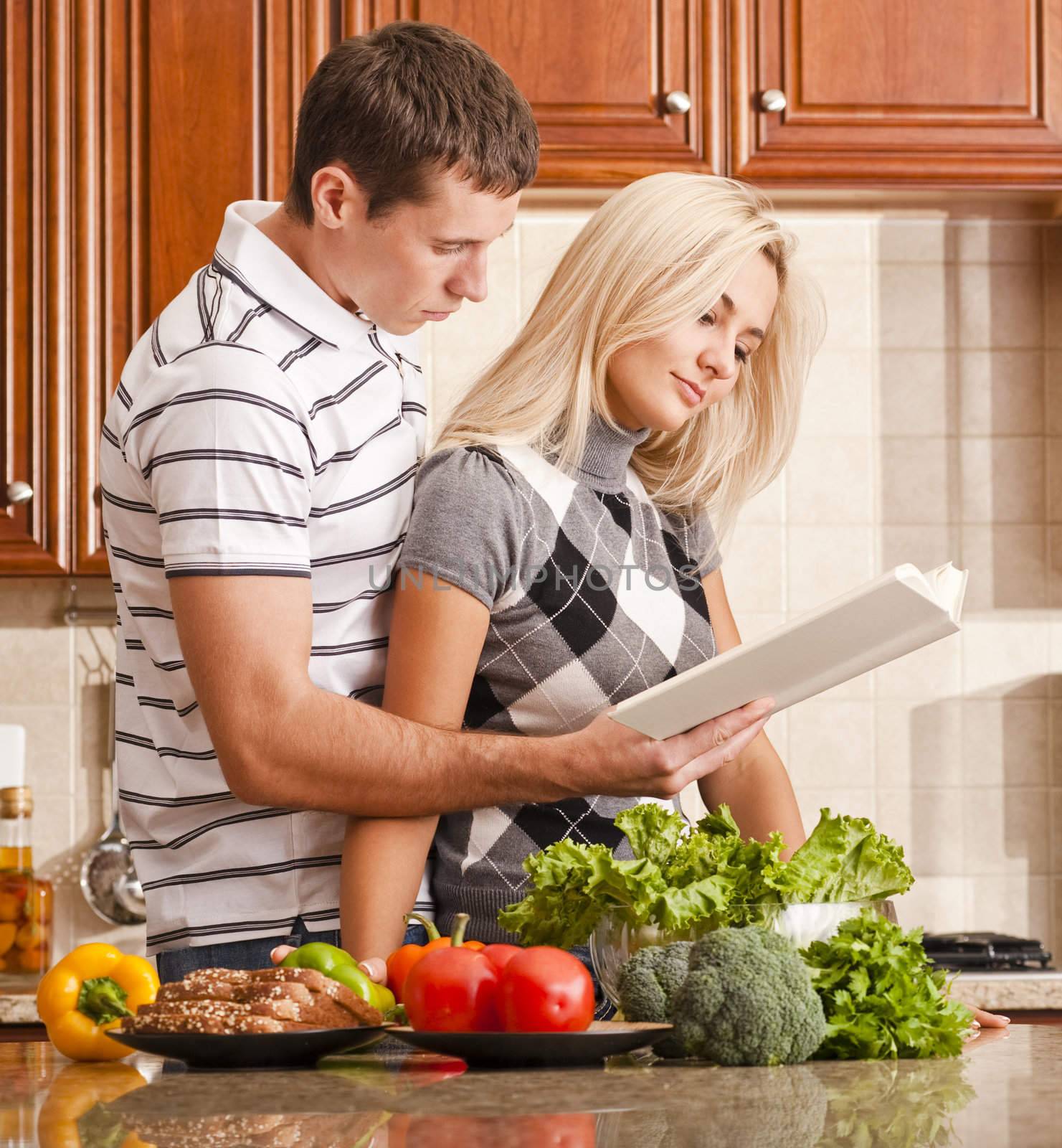Young couple read through a recipe book in the kitchen with a counter full of fresh vegetables. Square shot.