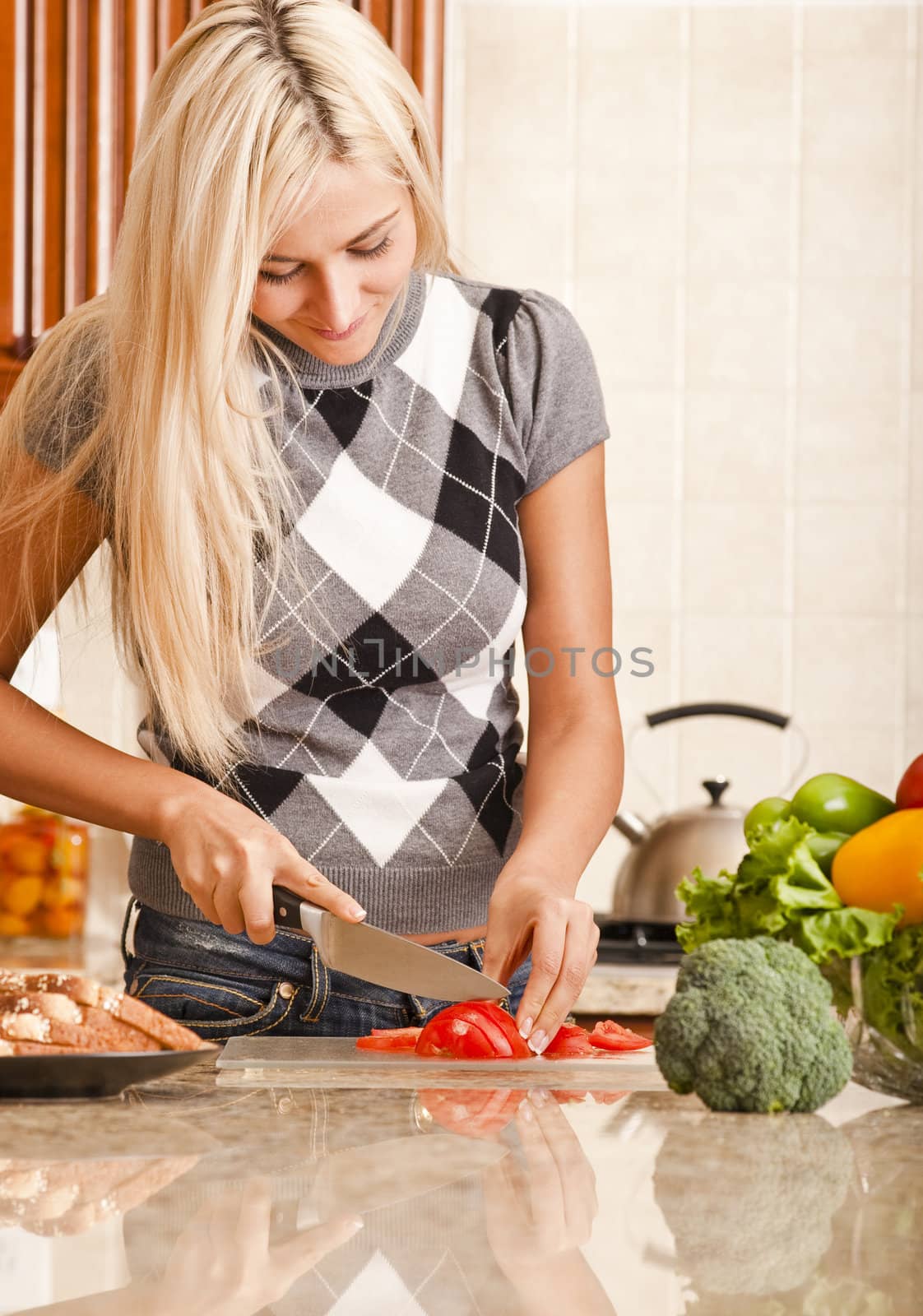 Young woman cutting up tomato in kitchen for meal. Vertical shot.