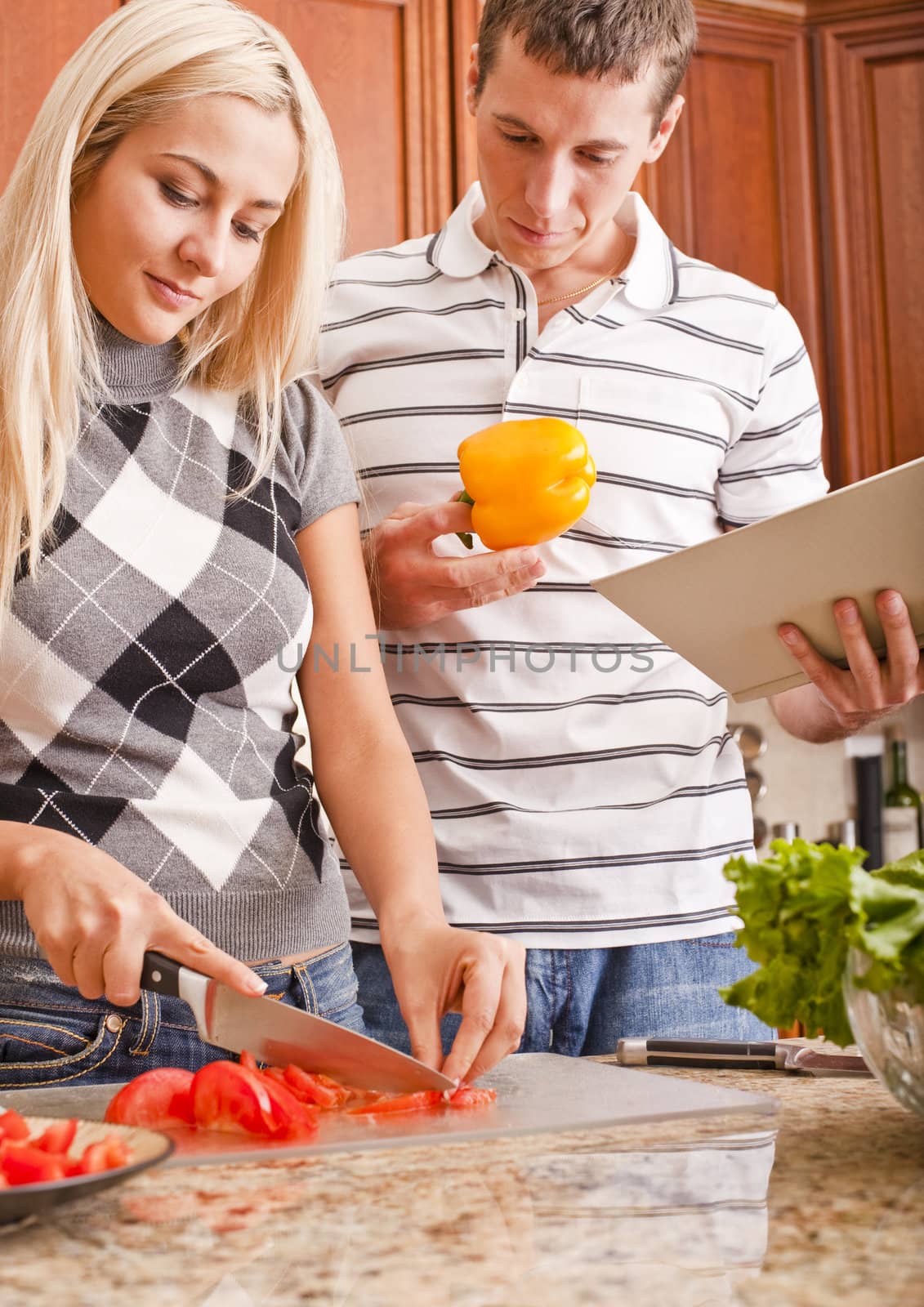 Young Man Holding Book Next to Woman Cutting Tomato by cardmaverick