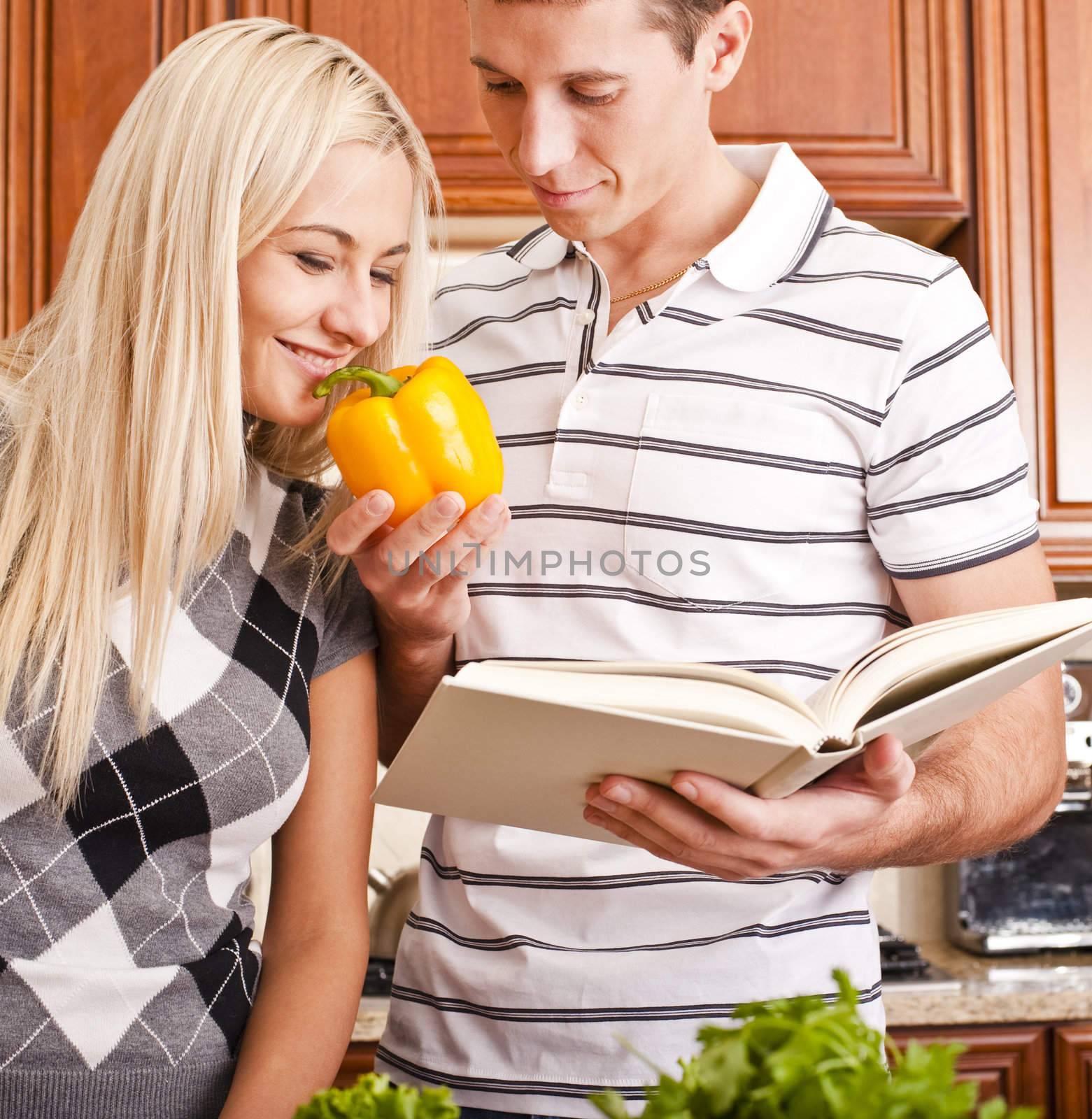 Young man with cook book holding yellow pepper for young woman to smell. Vertical shot.