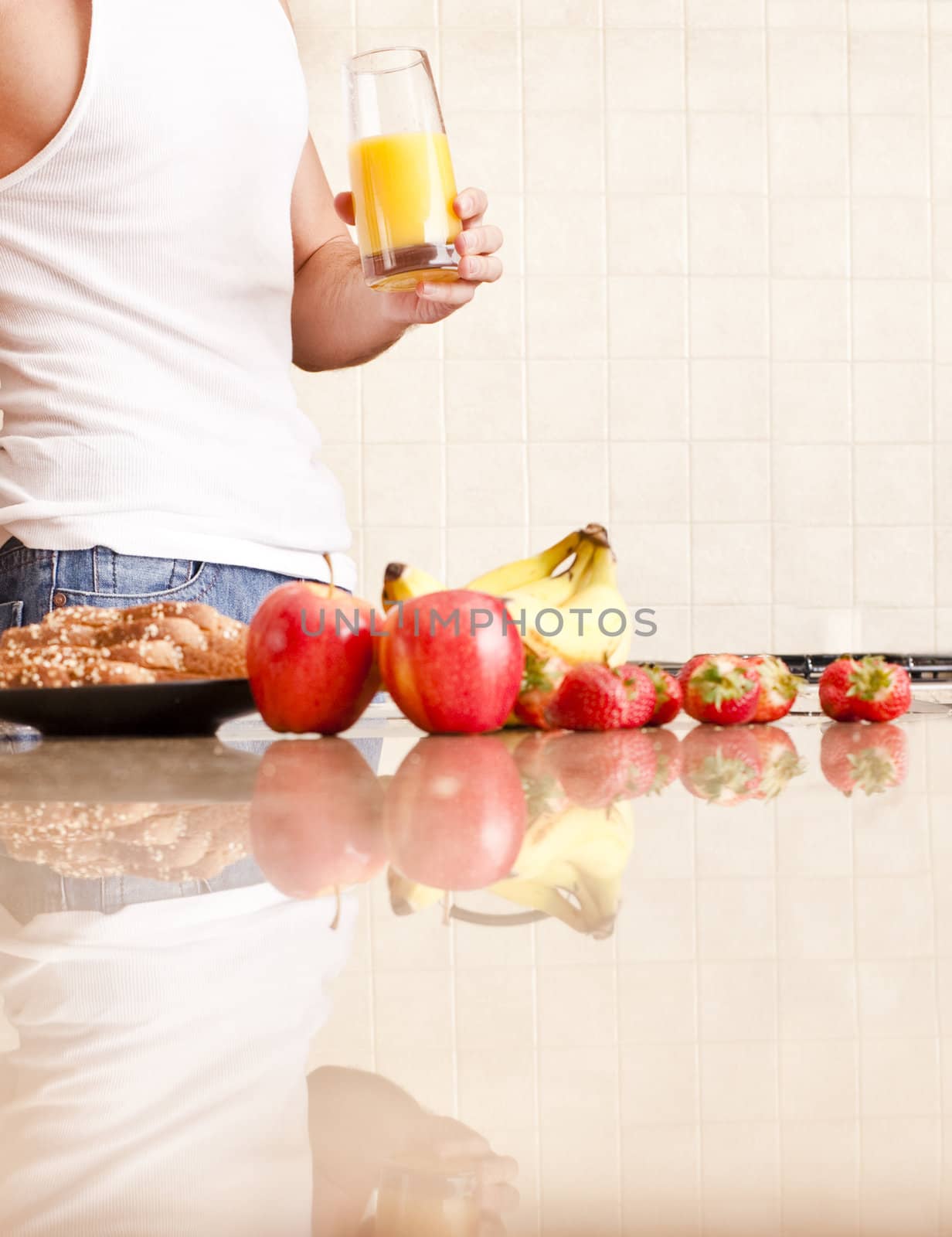 Young man wearing tank top and jeans in kitchen holding a glass of orange juice. Vertical shot.