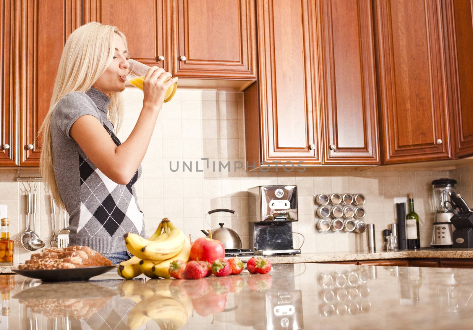 Young woman in kitchen drinking a glass of orange juice. Horizontal shot.