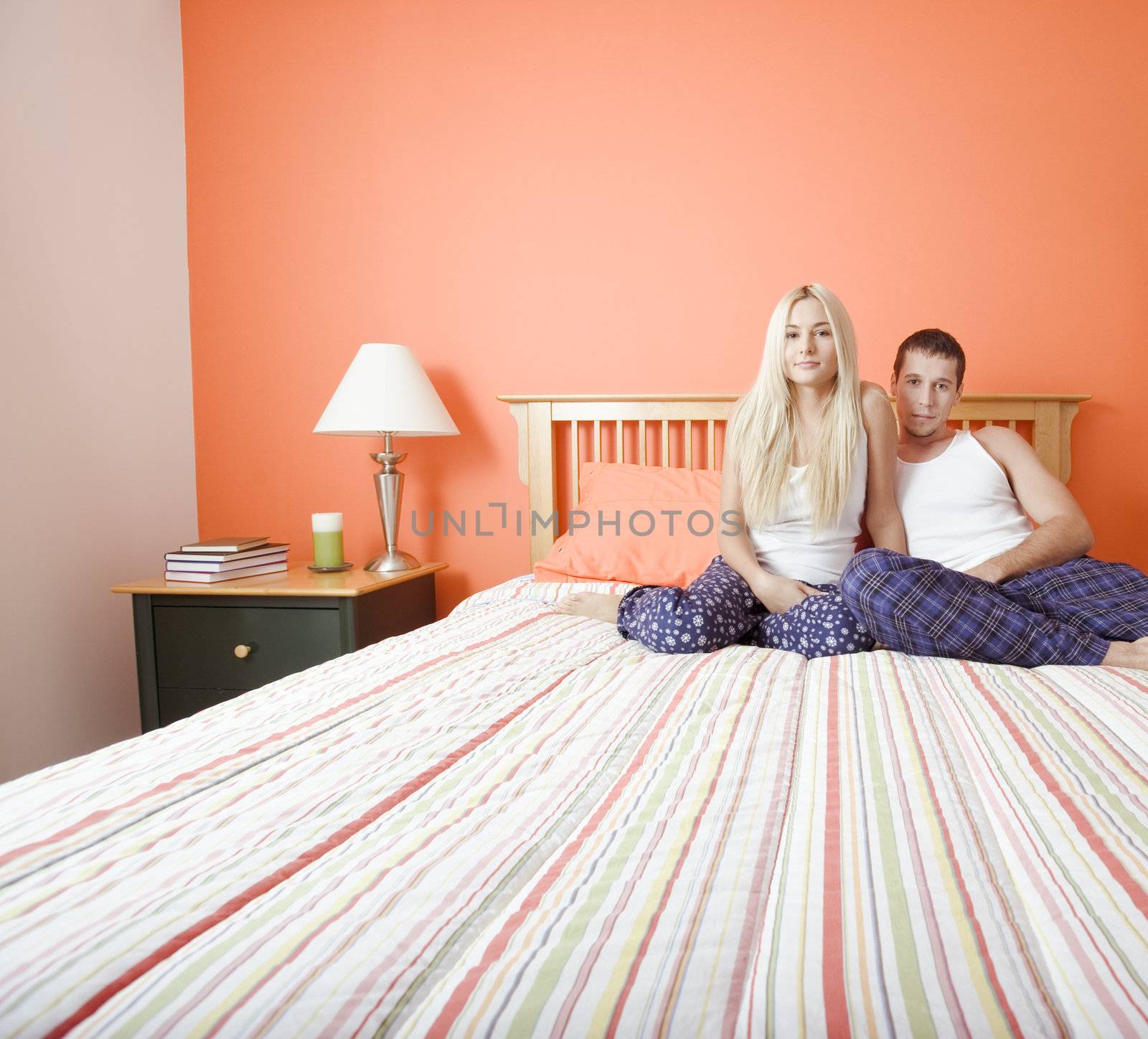 Young couple sitting on bed with stripped bedspread. Horizontal shot.