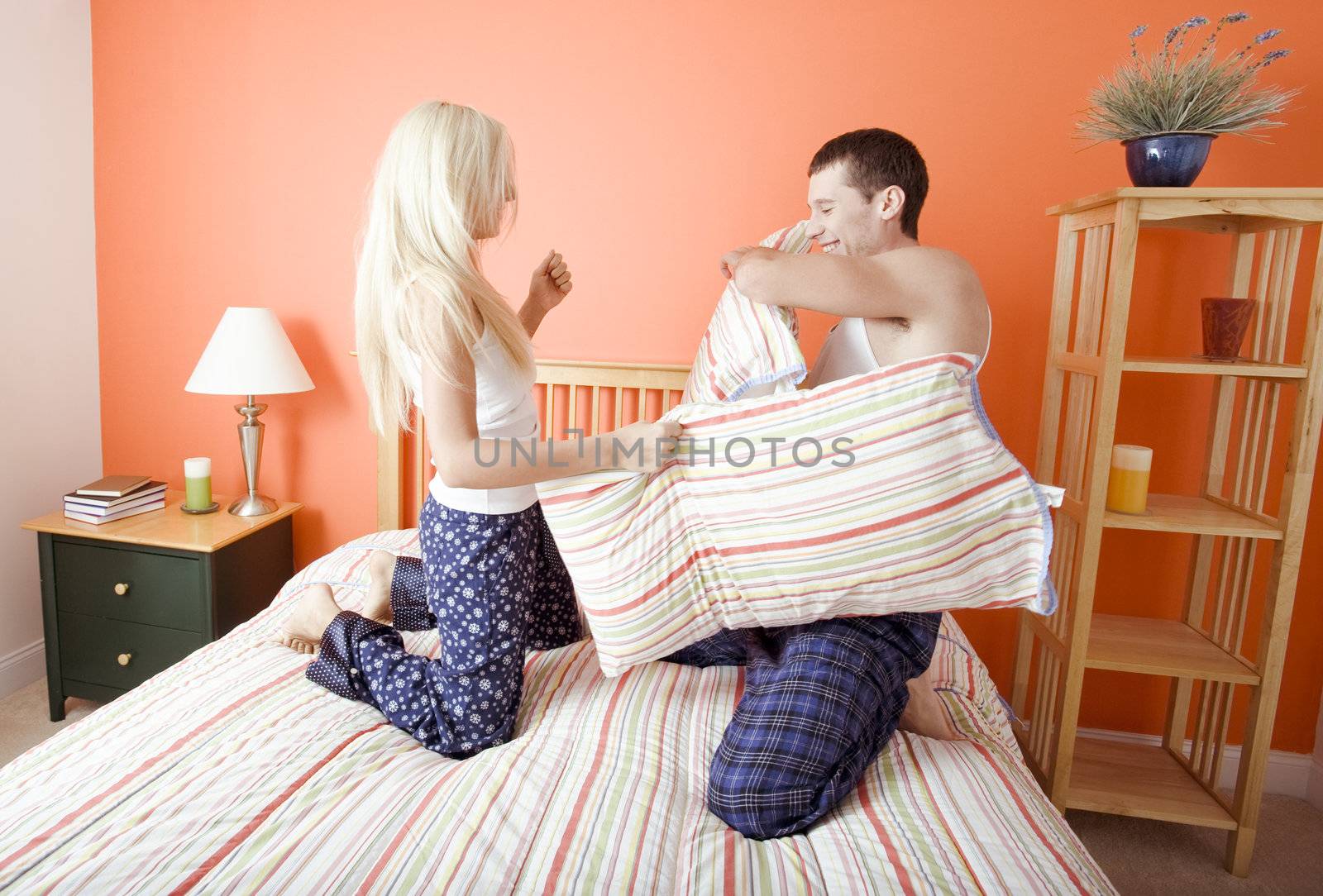 Young Couple Kneeling on Bed Having a Pillow Fight by cardmaverick