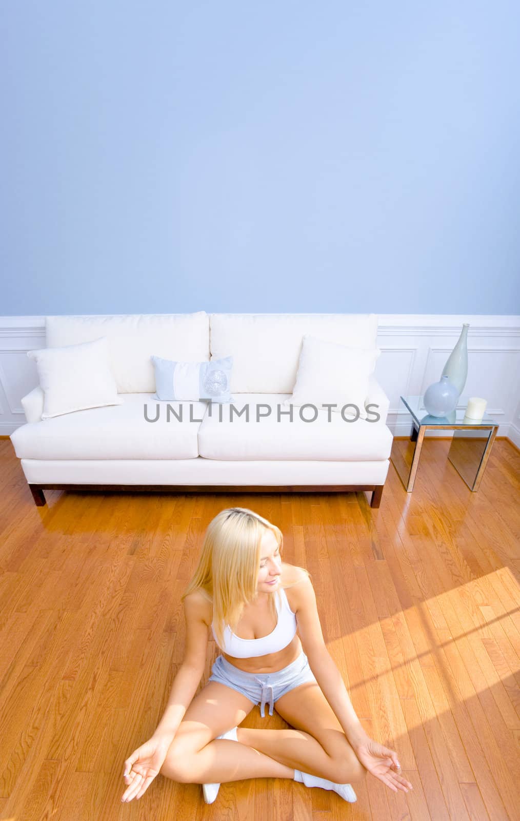 Young woman sitting cross legged on floor with hands on knees meditating. Vertical shot.