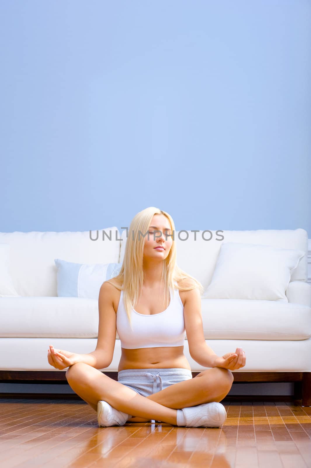 Young woman sitting cross legged on floor with hands on knees meditating. Vertical shot.