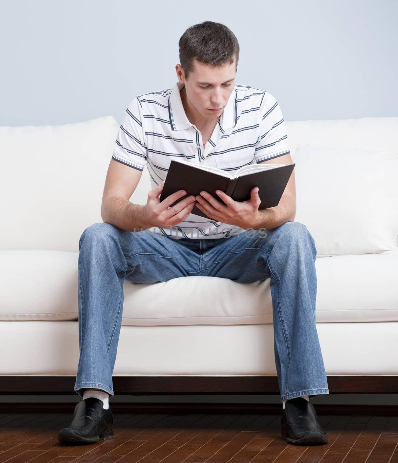 Young Man Sitting on Sofa Reading by cardmaverick