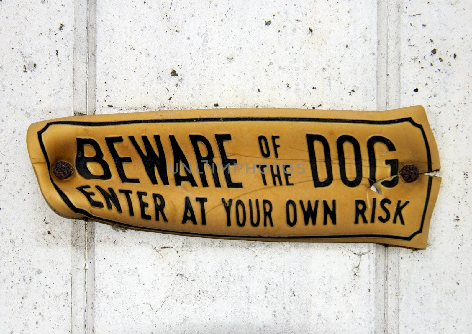 A grungy, distorted, 'Beware of the Dog' sign, nailed to a wooden gate. Clipping path, around the sign, included so it can be extracted and placed on any other background.