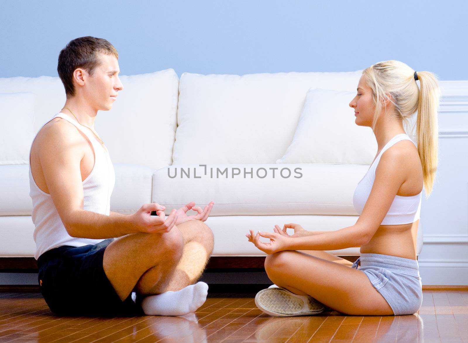 Young couple in sportswear face each other as they meditate on the floor. Horizontal shot.