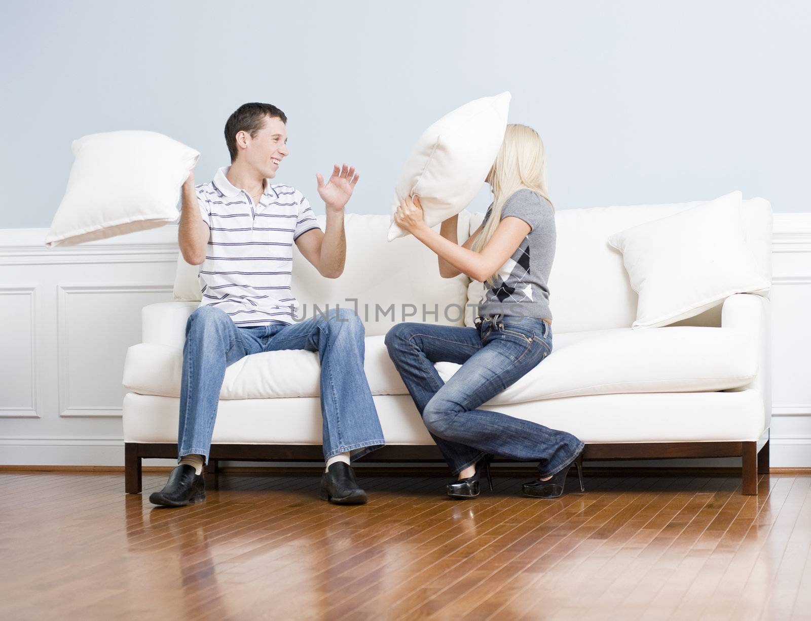 Young couple laugh while having a pillow fight on the sofa. Horizontal shot.