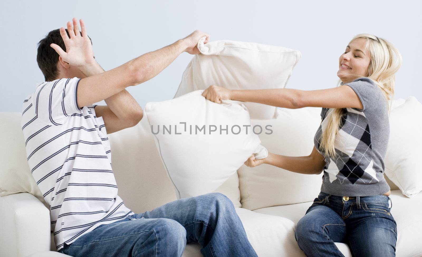 Young man holds his arm up in defense as a young woman playful hits him with a pillow. Horizontal shot.