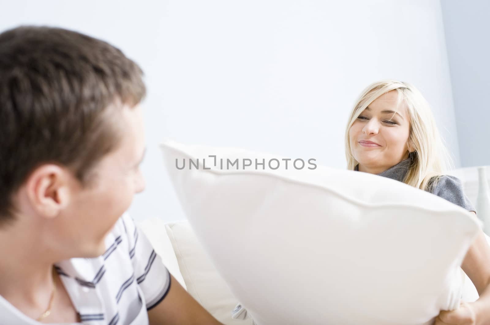 Young woman hits a young man with a pillow as he attempts to get away. Horizontal shot.