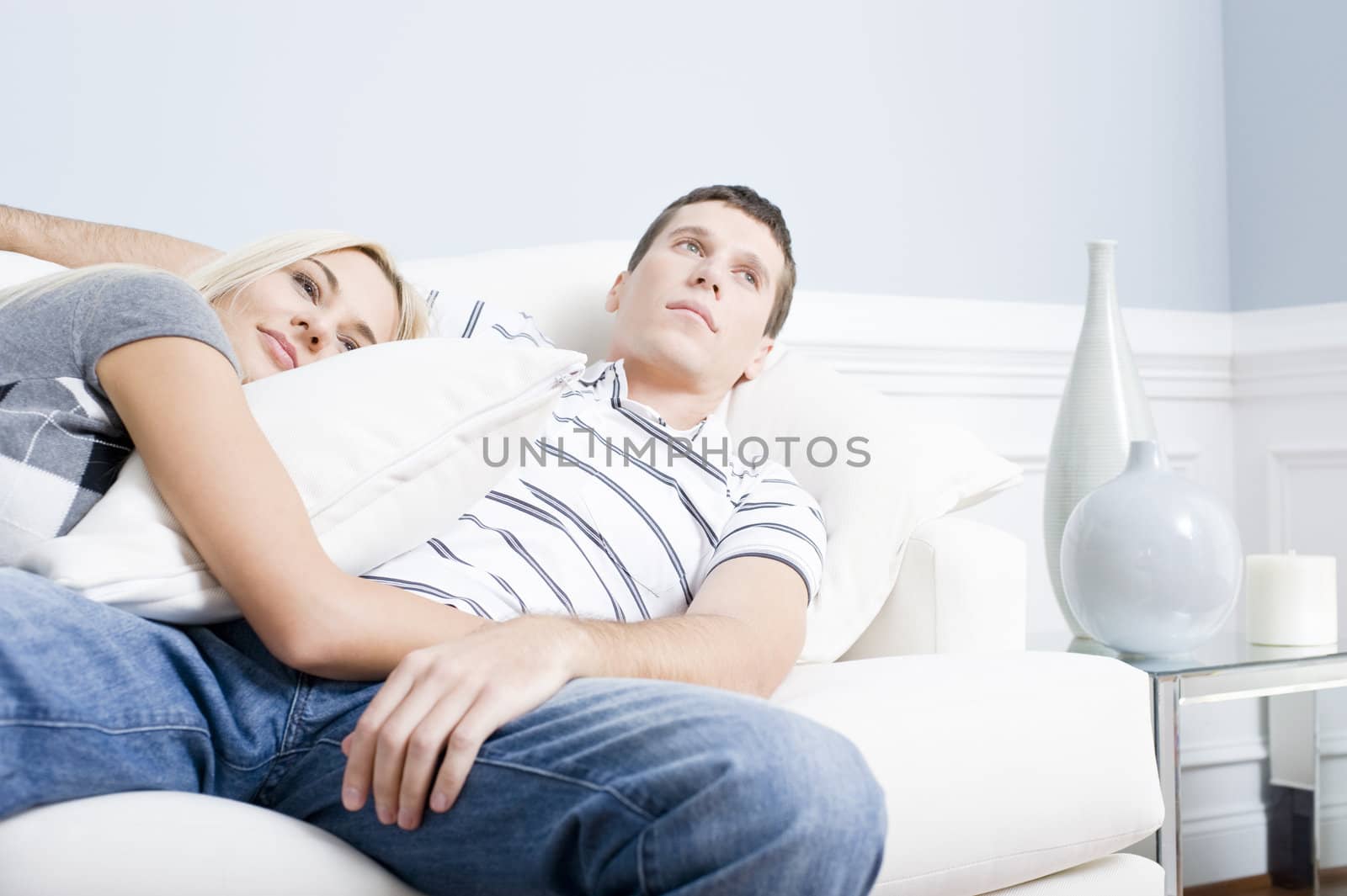 Woman snuggles up to man as they both relax quietly on a white couch. Horizontal format.