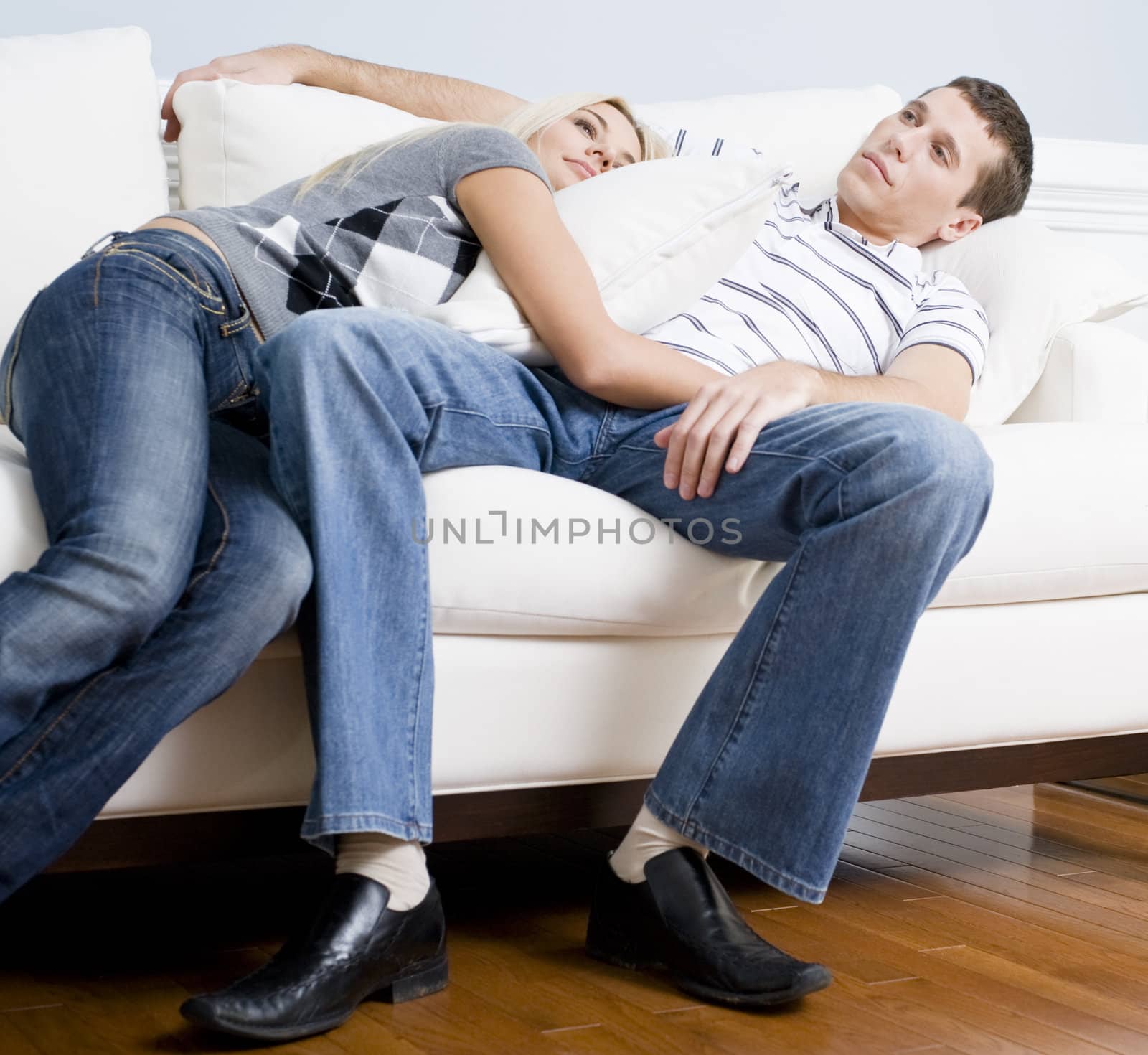 Woman snuggles up to man as they both relax quietly on a white couch. Horizontal format.