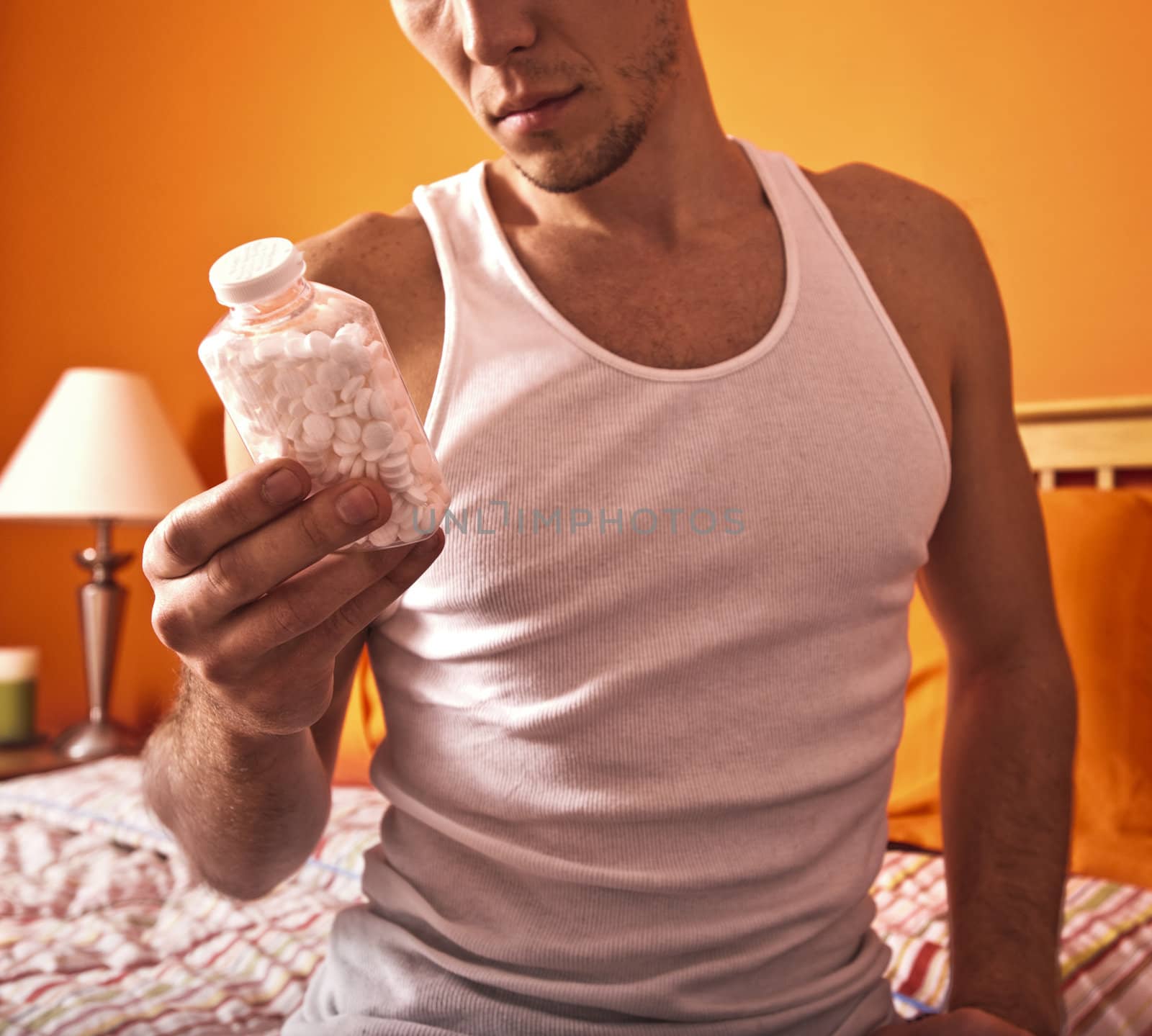 Cropped view of man sitting on his bed and looking at a bottle of pills. Square format.