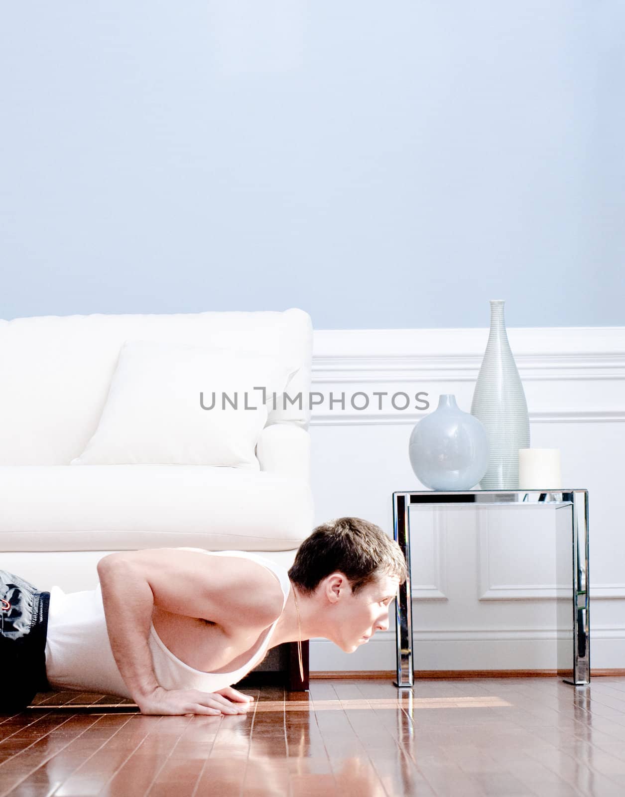 Cropped view of man doing push-ups next to couch. Vertical format.