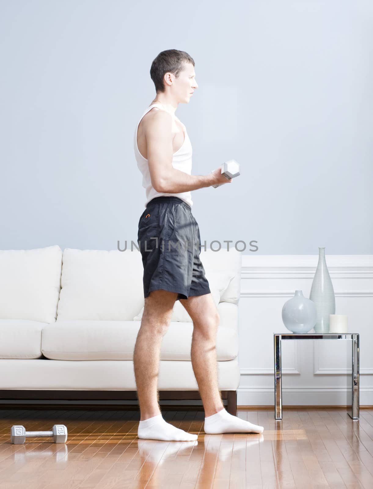 Man using arm weight in his living room as another lies on the floor next to him. Vertical format.