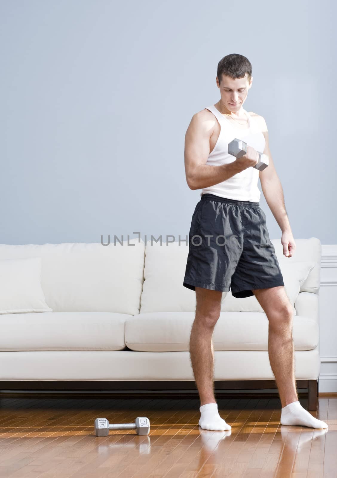 Man using arm weight in his living room as another lies on the floor next to him. Vertical format.