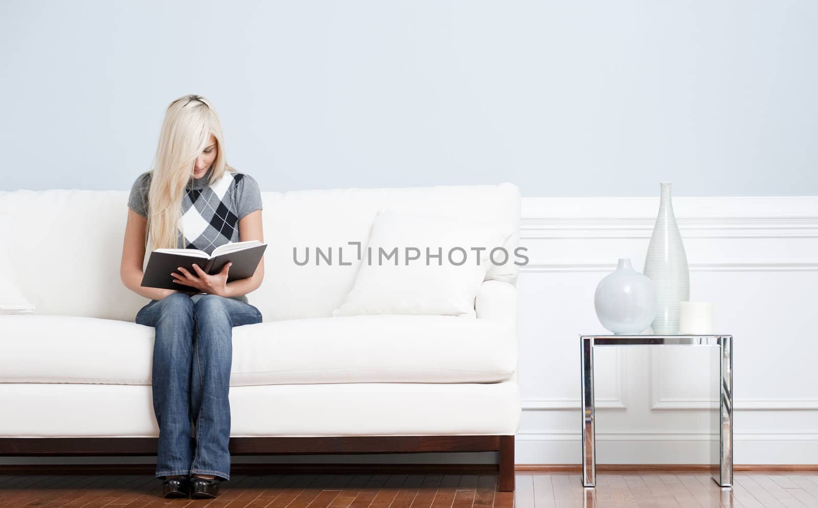 Full length view of woman sitting on a white couch with a book. Horizontal format.