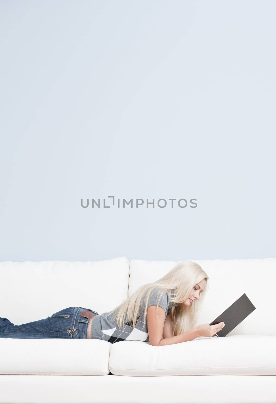 Cropped view of woman lying on white couch and reading a book. Vertical format.