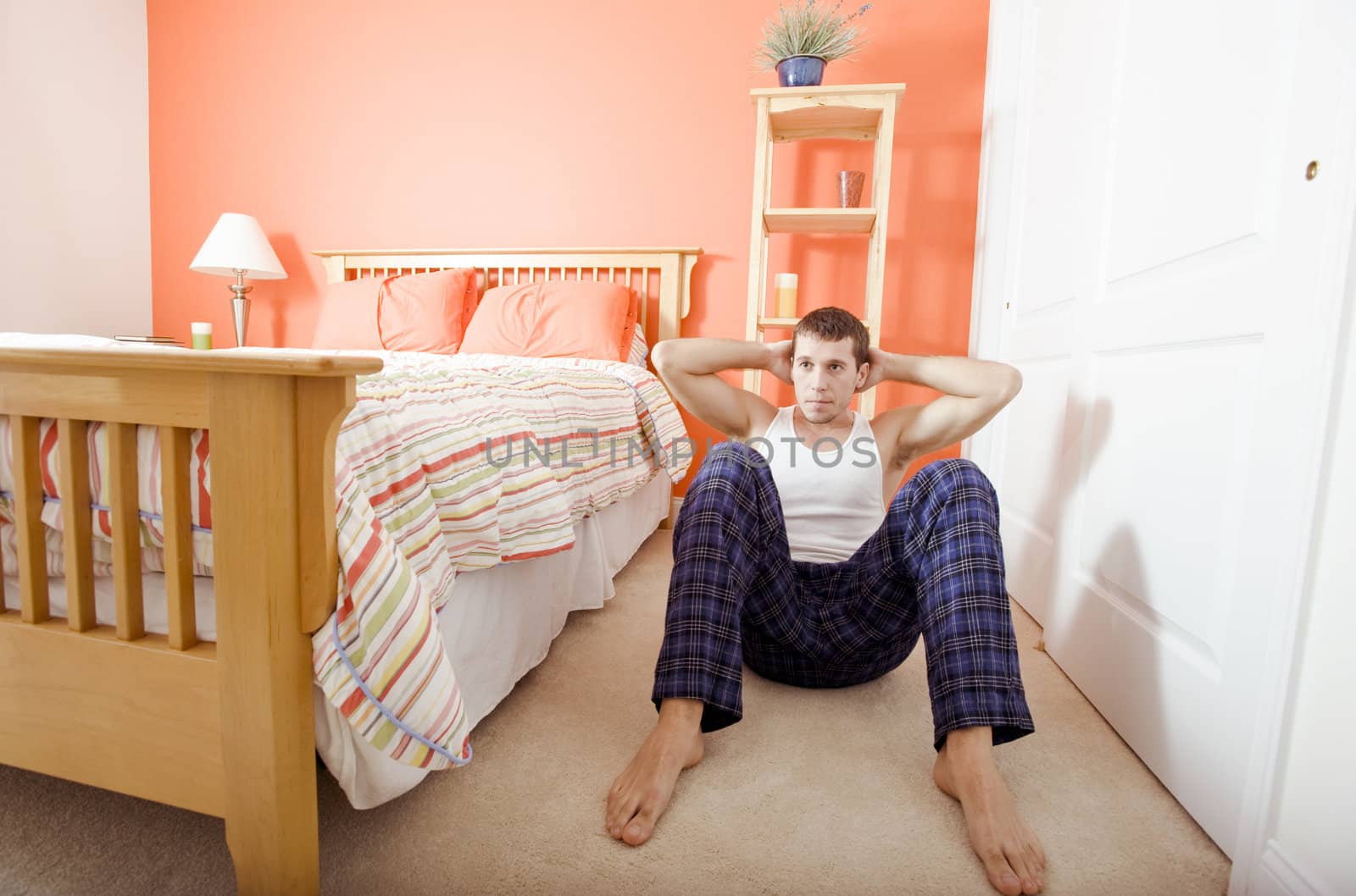 View of man facing the camera and doing sit-ups next to his bed. Horizontal format.