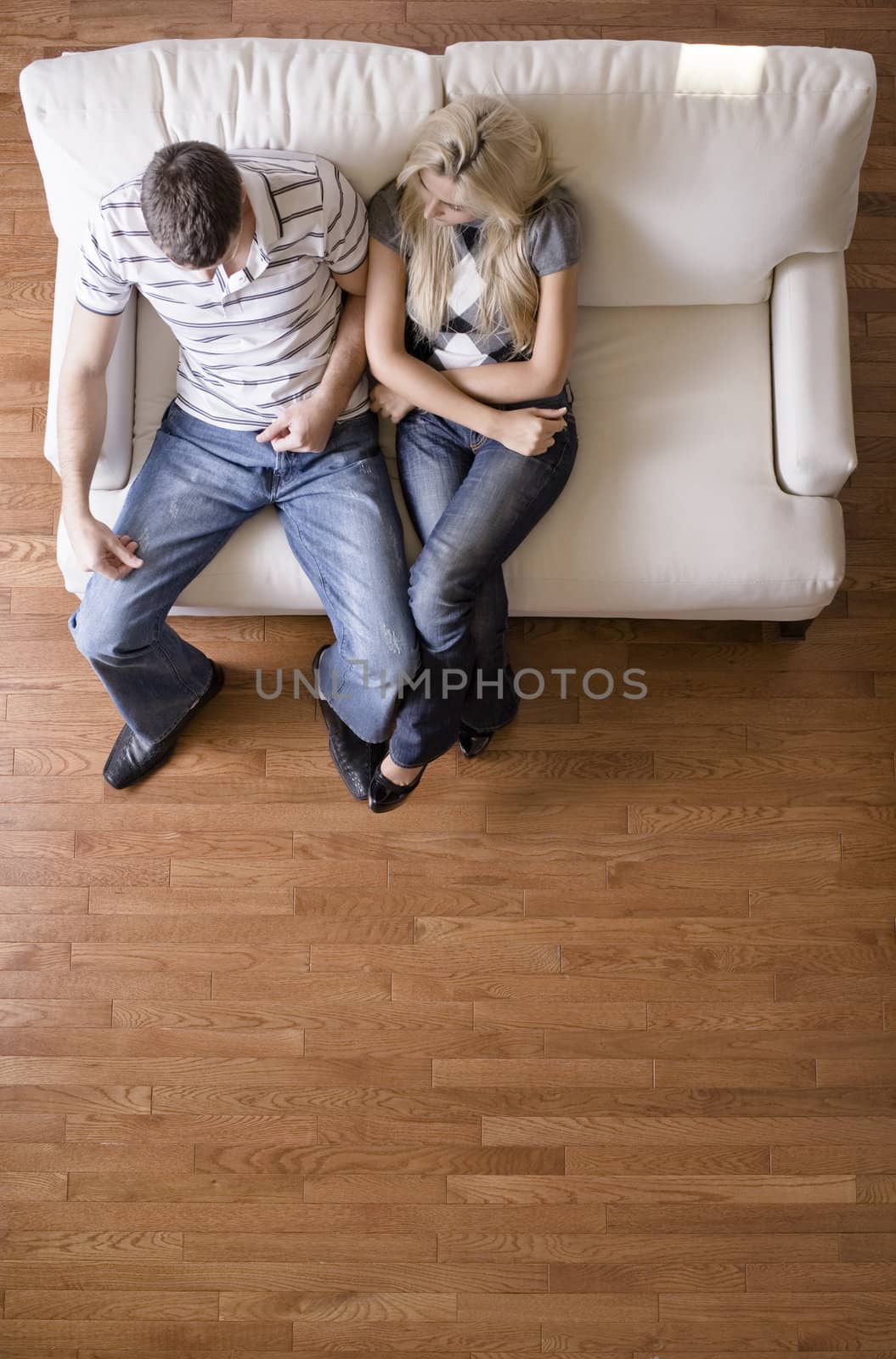 Full length overhead view of couple sitting together on white love seat. Vertical format.