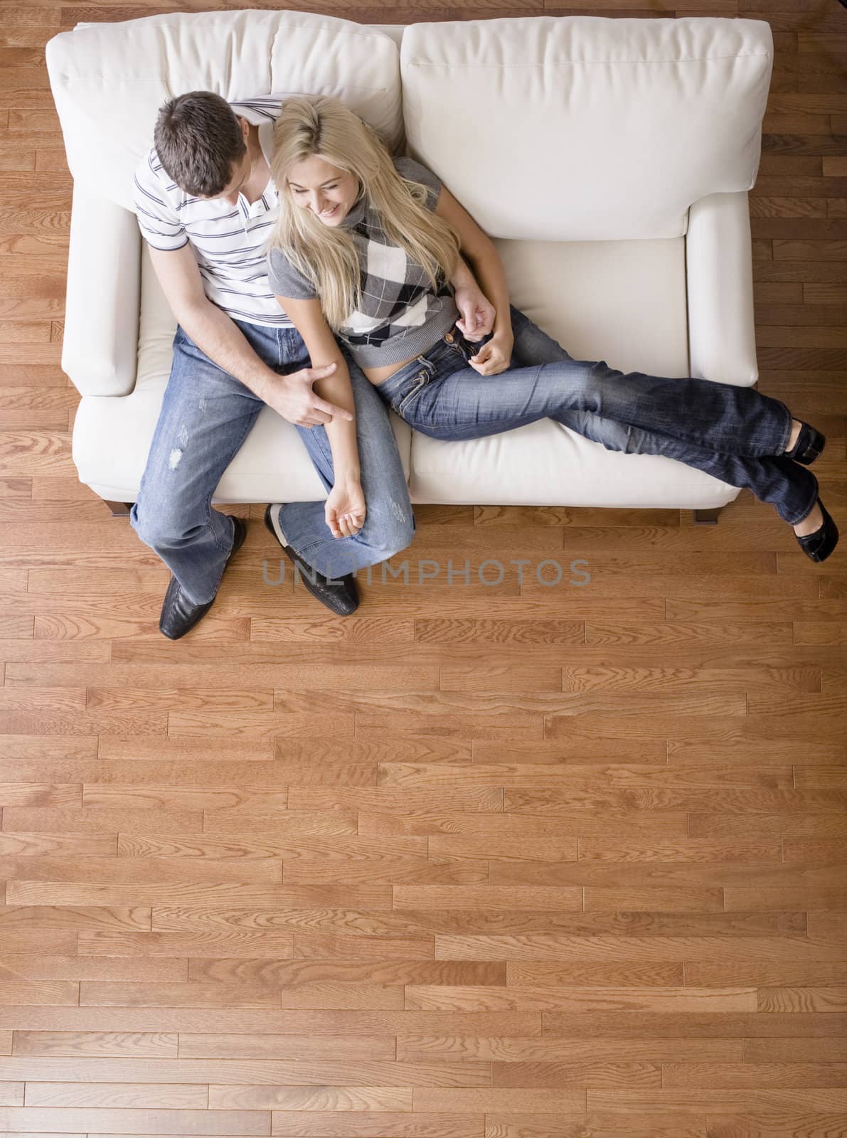 Full length overhead view of affectionate couple sitting together on white love seat. Vertical format.